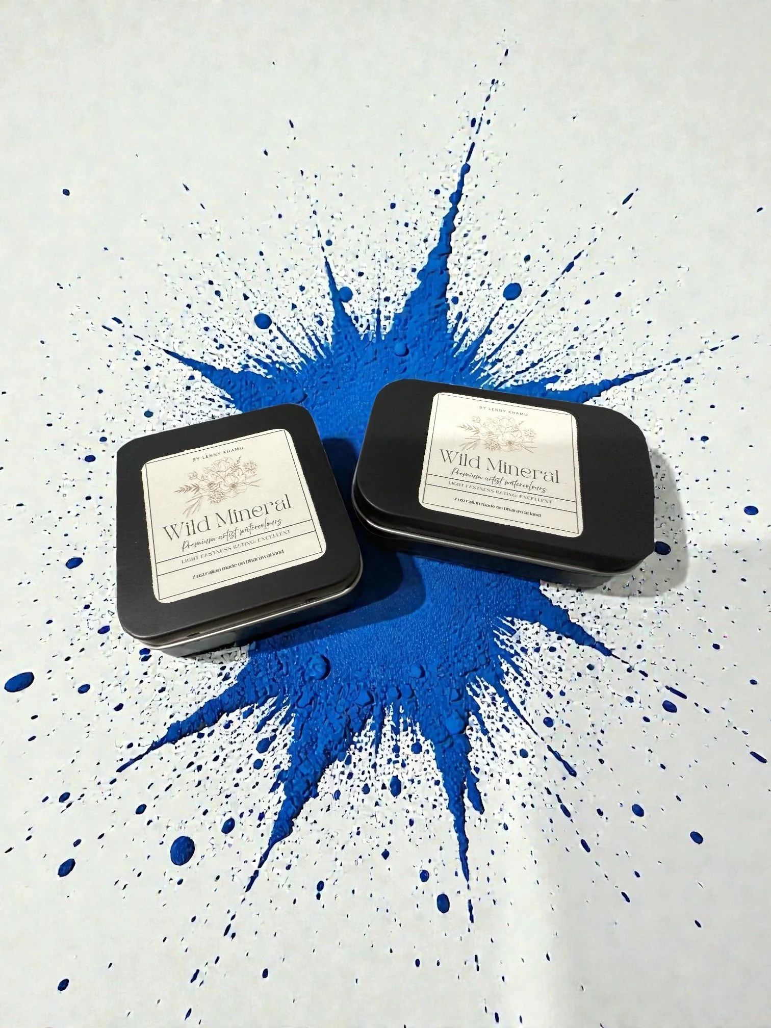 Two black tins labeled 'Wild Mineral' placed on a white surface with blue paint splash design.