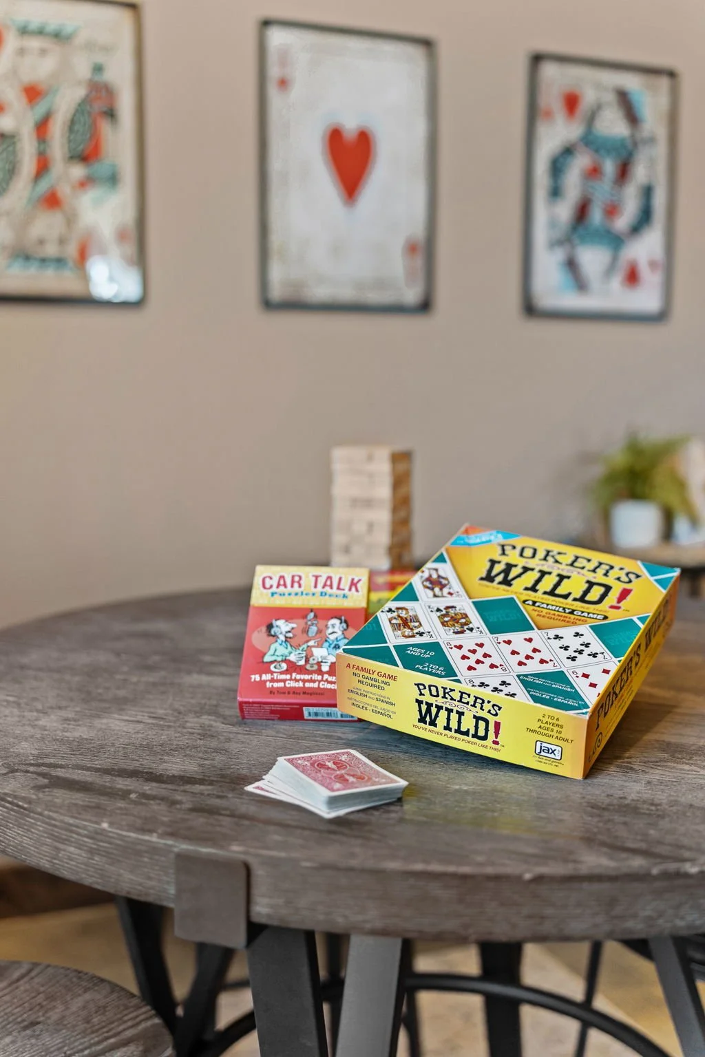 Table with card games and a deck of cards, with framed playing card artwork on the wall in the background.