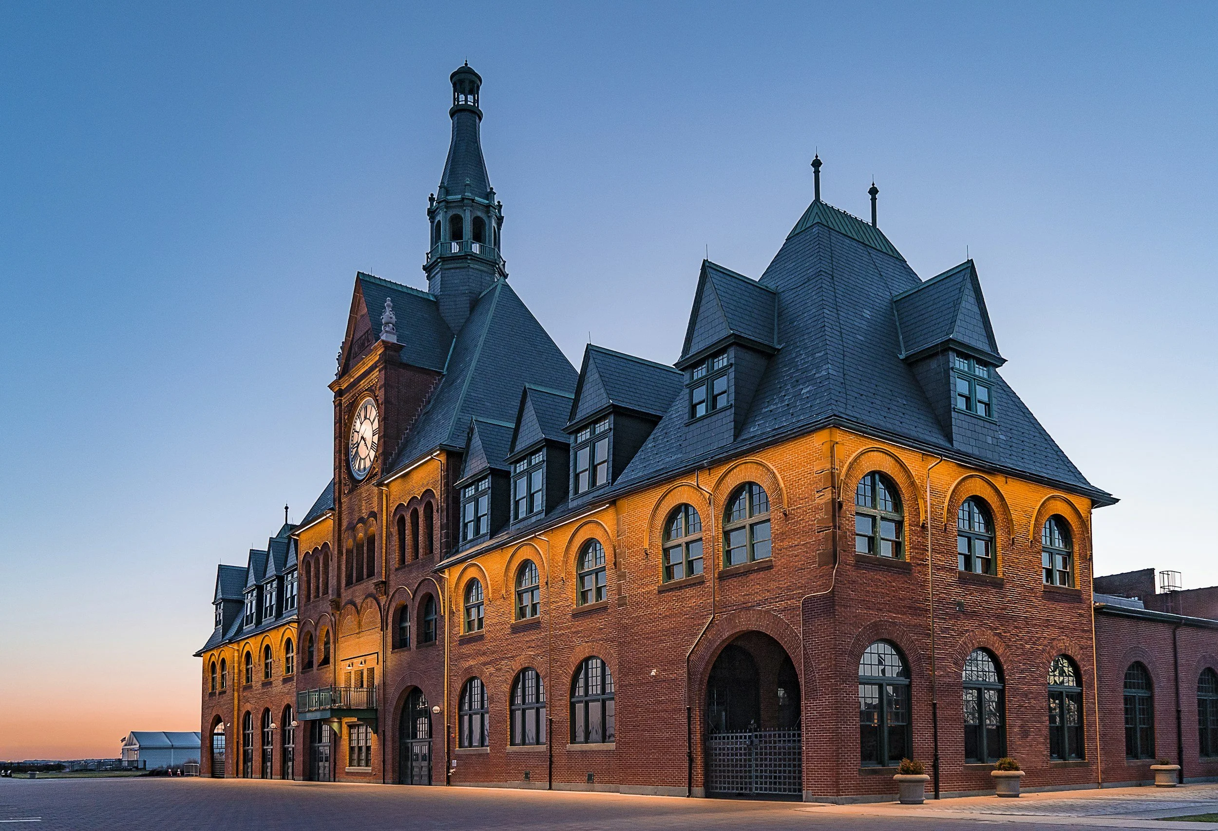 Historic red brick building with a clock tower and steep dark roofs at sunset.
