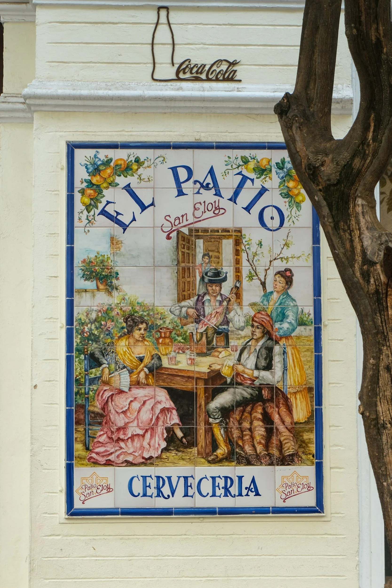 Decorative tile sign for a Spanish cervecería depicting people in traditional clothing enjoying drinks, with the words "El Patío San Eloy" and "Cervecería".