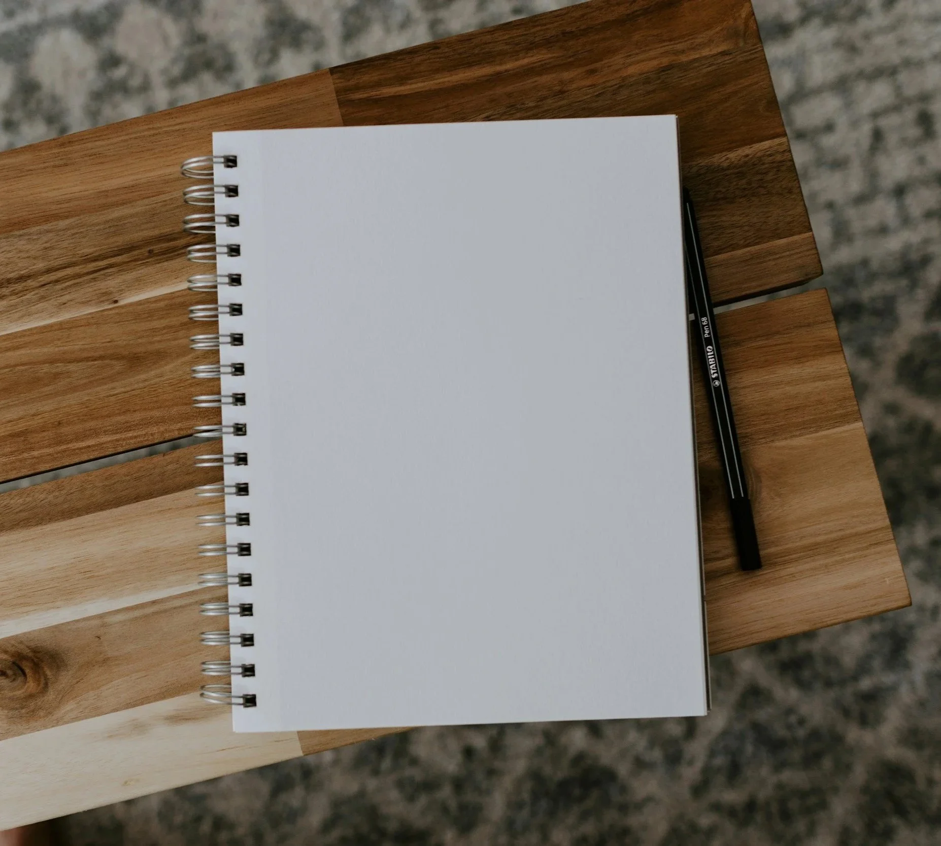Open spiral-bound notebook with blank white pages placed on a wooden table, accompanied by a black ink pen.