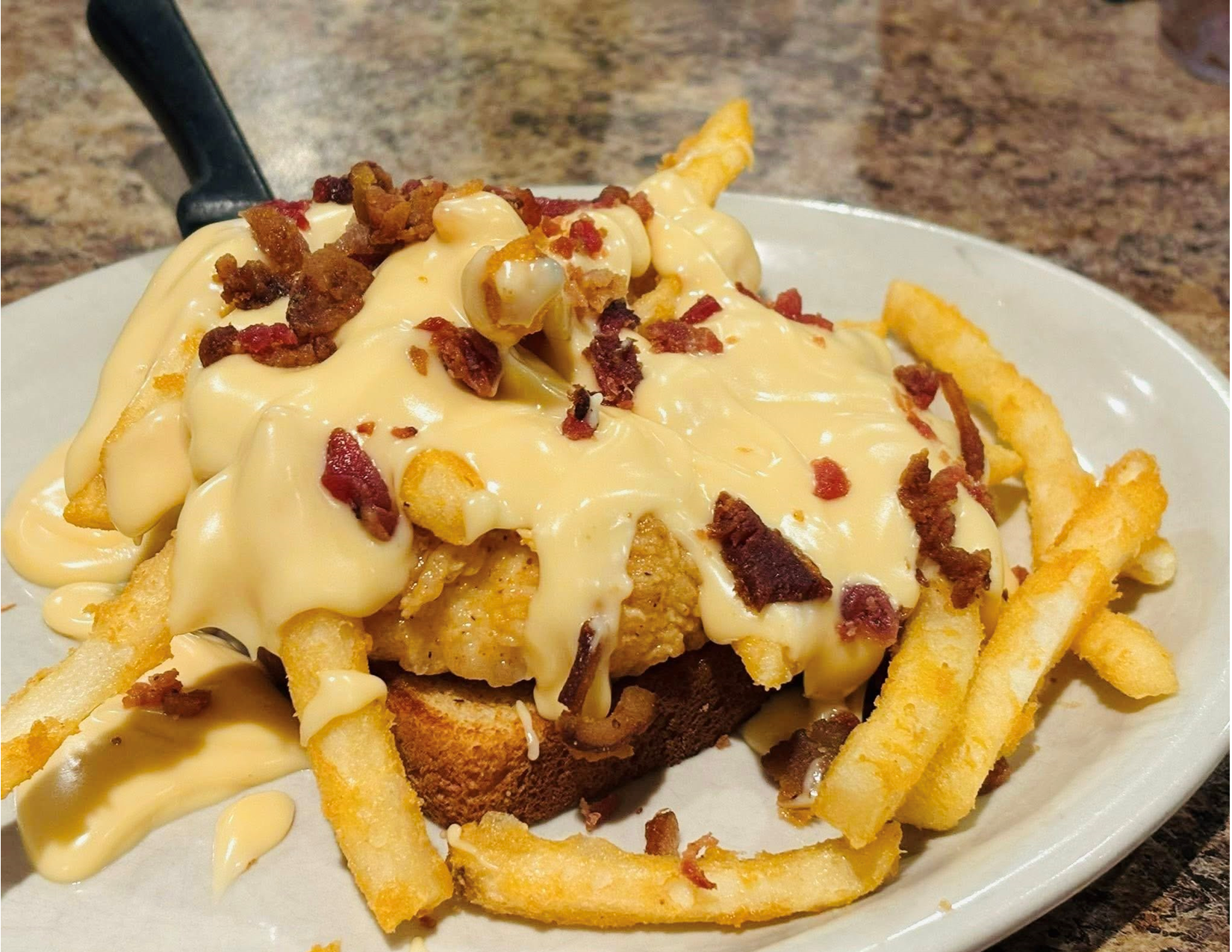 French fries topped with gravy, cheese, bacon bits, and chopped bacon on a white plate.