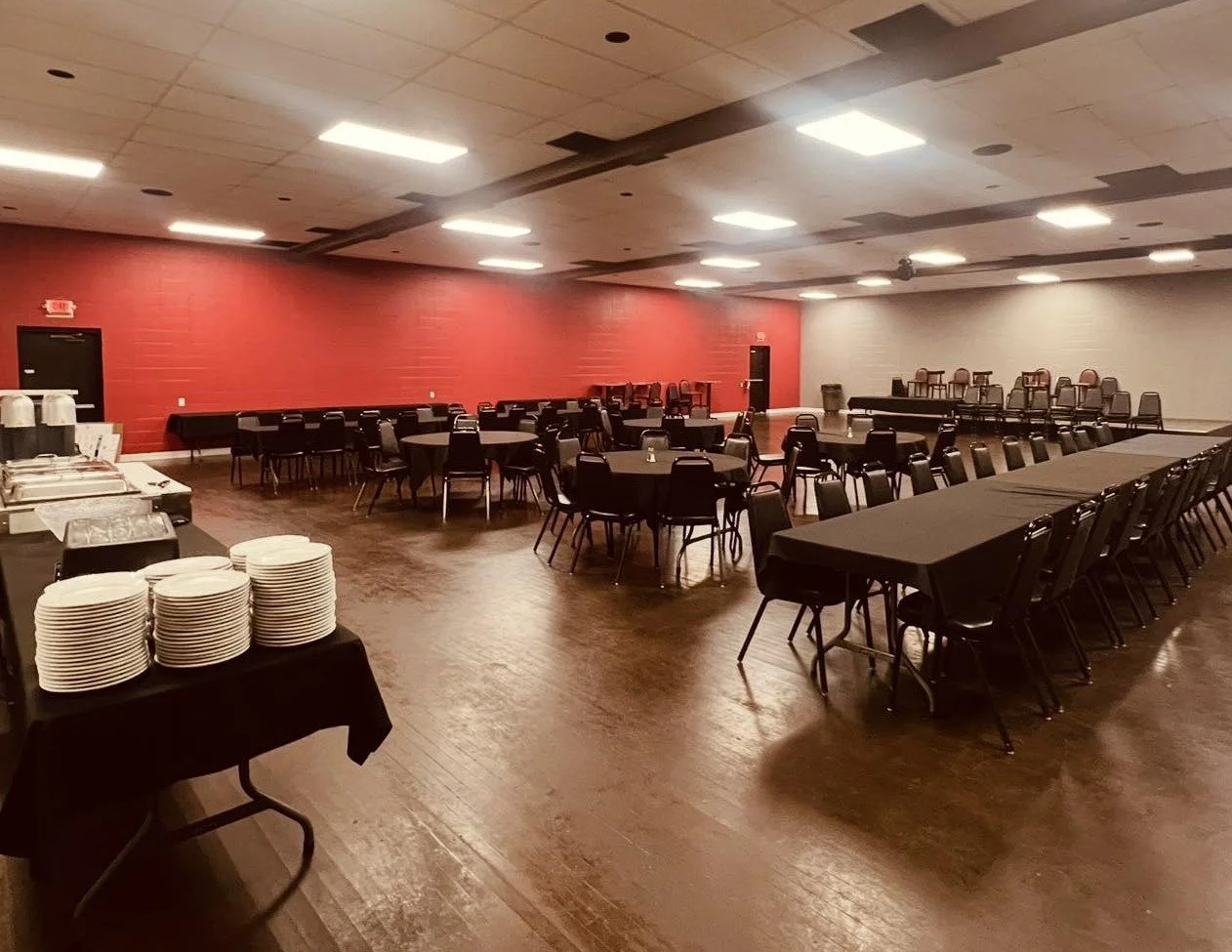 Event banquet hall setup with tables, chairs, and a serving station with plates and coffee dispensers.