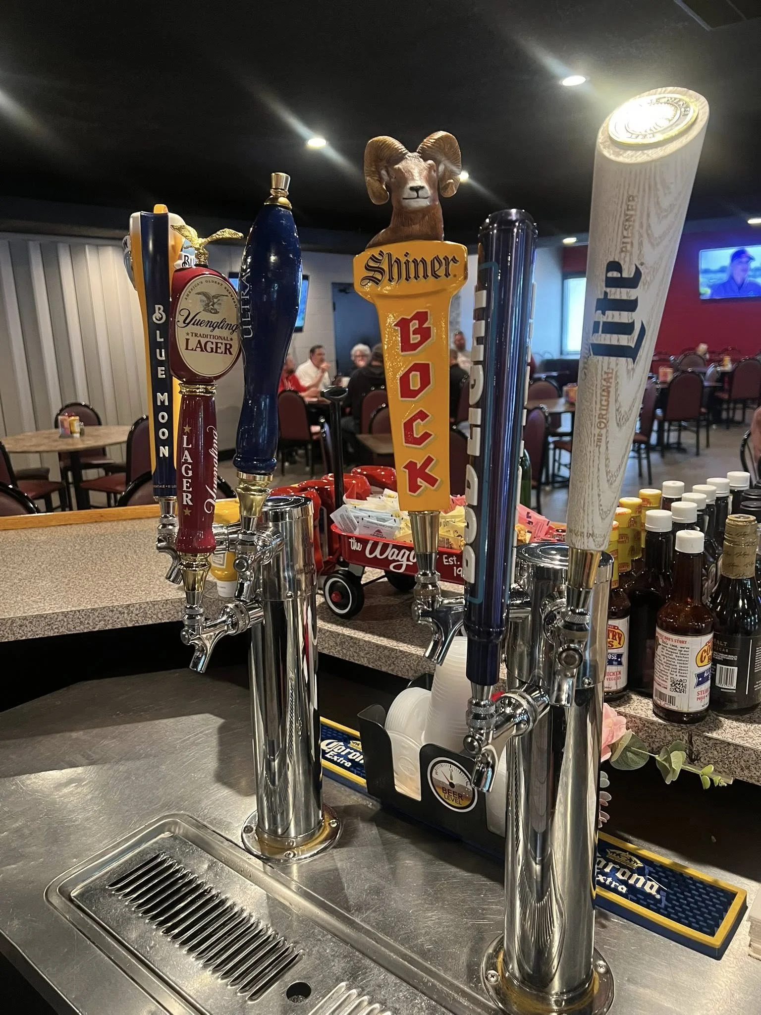 View of bar taps for different beers, including labels for Blue Moon, Yuengling Lager, and Miller Lite, with a ram's head decoration on one tap, in a bar or restaurant setting.