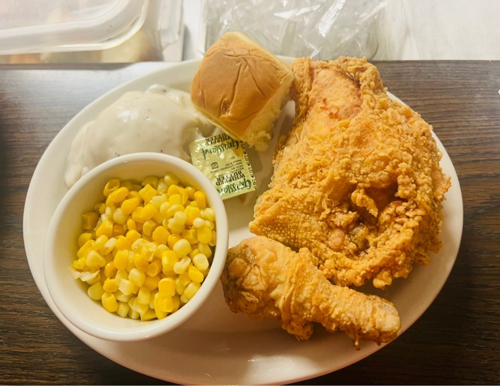 Plate of fried chicken, a biscuit, mashed potatoes with gravy, a serving of corn, and a pat of butter.
