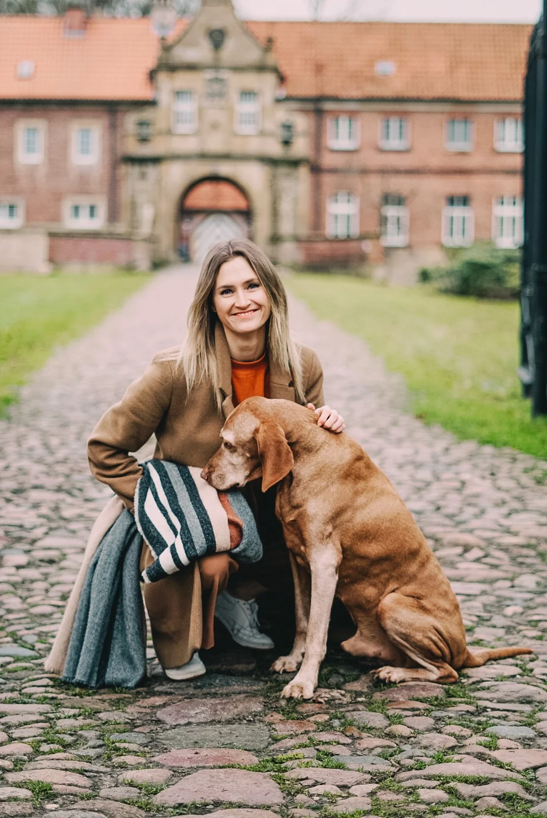 Lächelnde Frau mit braunem Hund vor einem historischen Backsteinschloss