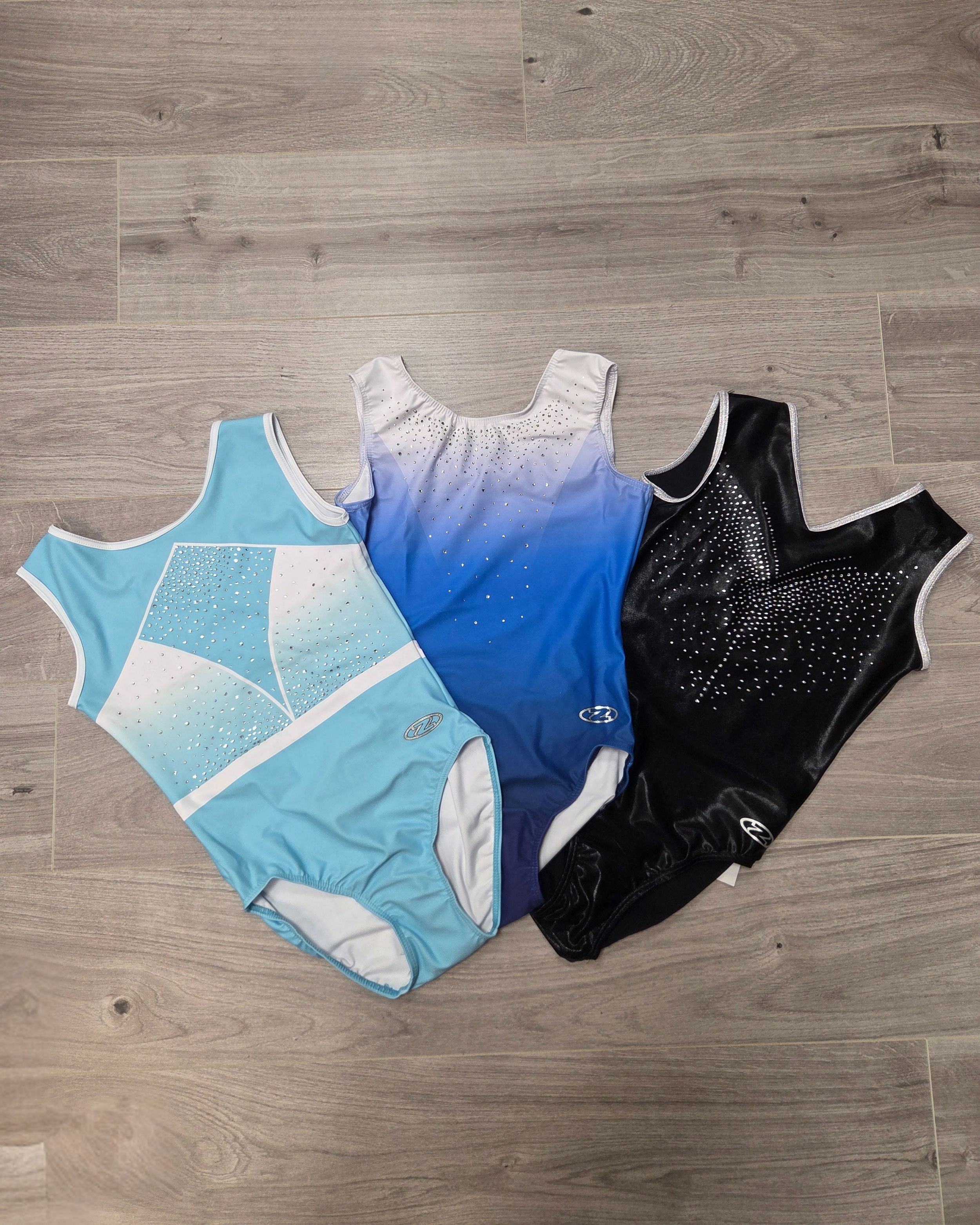 Three gymnastics leotards in acqua, blue and shiny black. All have diamanté detailing.