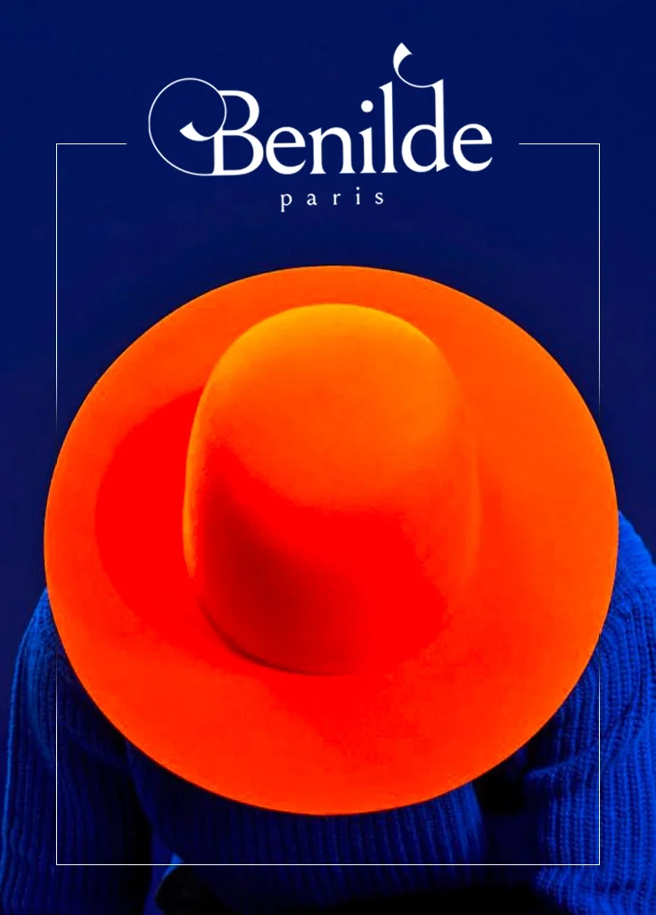 Une image d'une personne portant un chapeau orange vif, avec en arrière-plan un fond bleu foncé. En haut, il y a le logo et le nom 'Benilde Paris' en blanc.
