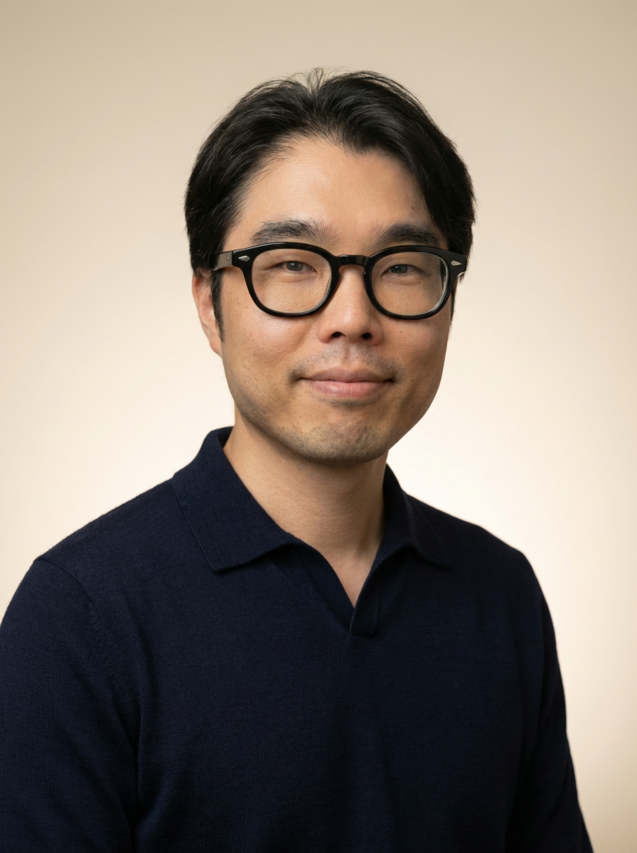 Portrait of a man with black hair, glasses, and a slight smile, wearing a dark navy polo shirt, against a neutral background.