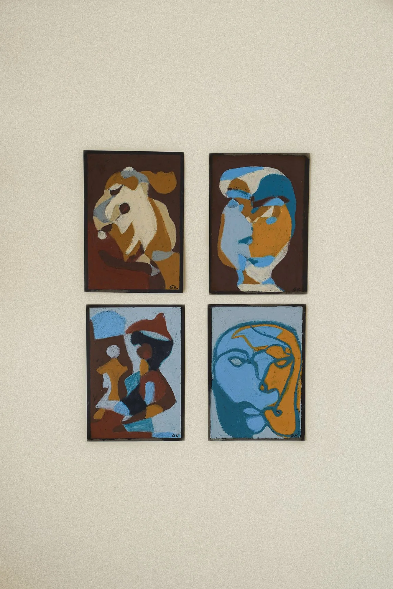 Four figurative abstract paintings of human faces and figures arranged on a beige wall, in an art studio in Oslo. 