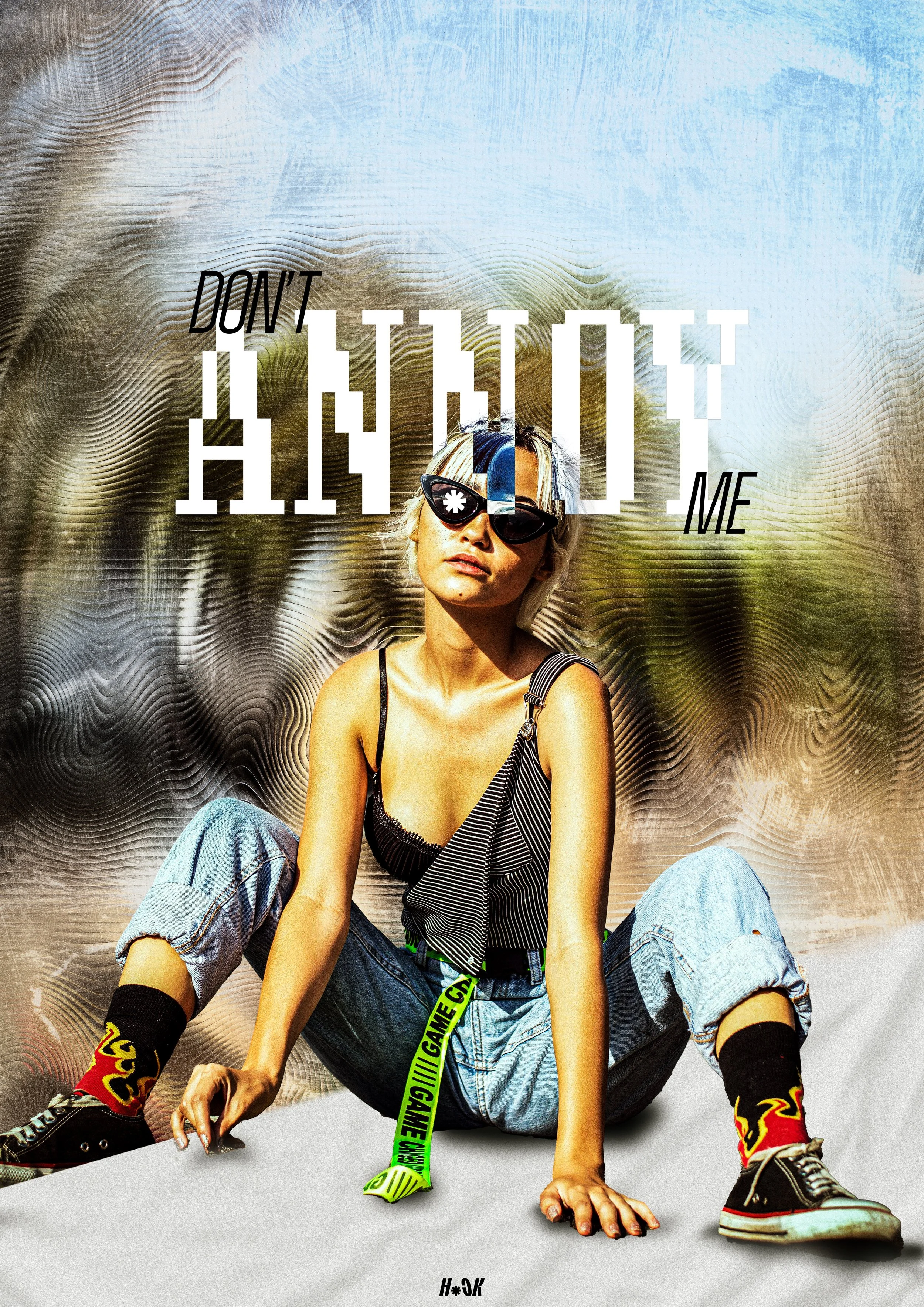 A young woman with blonde hair wearing sunglasses, a black and white striped top, loose jeans, colorful socks, and sneakers, sitting on the ground outdoors with a blurred background of trees and sky. Overlaid text says, 'Don't attack me' in stylized 