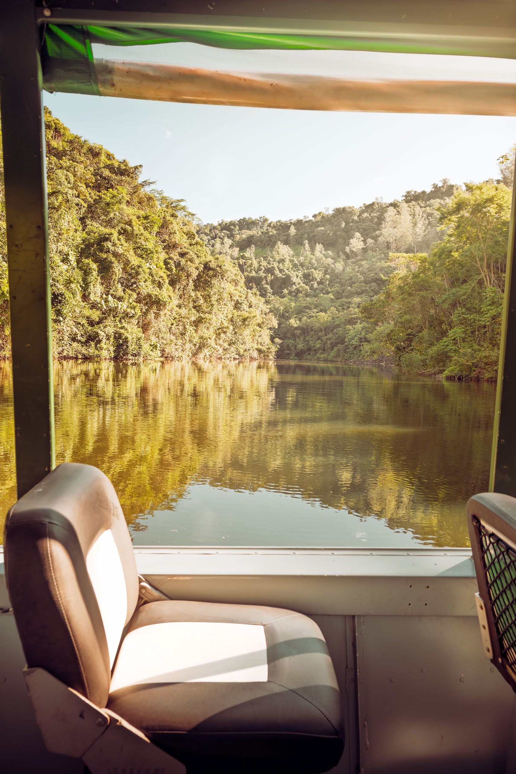 Assento de barco enquadrando a represa do Legado das Águas com colinas verdes e luz suave da tarde. Reflexo uniforme na água. Ideal para decoração com foco em calma e natureza tropical.
