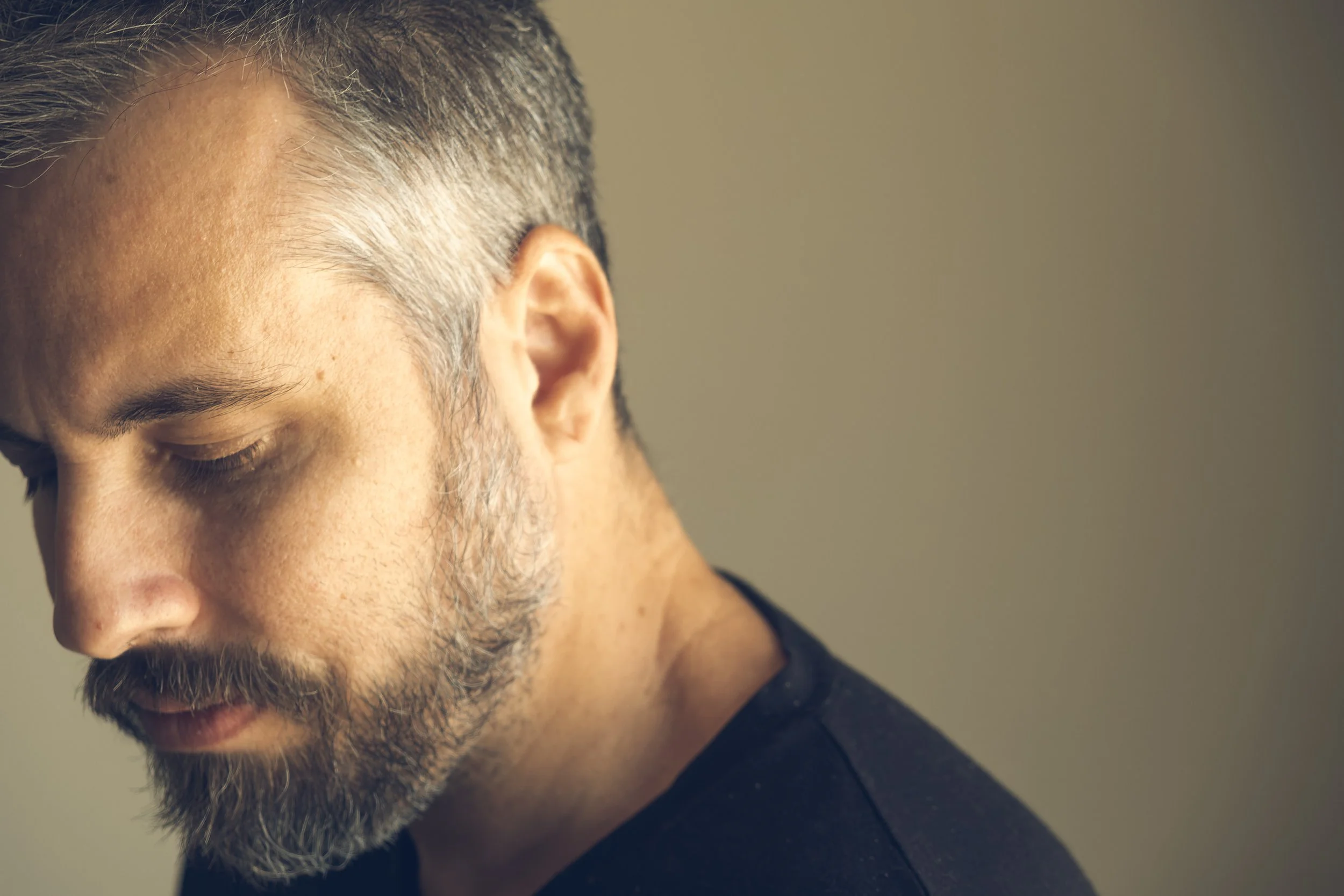 Retrato de Pedro Ferr em perfil com luz suave lateral, cabelo grisalho curto, barba curta e expressão séria, fundo neutro creme. Fotografia usada no site de quadros fine art e na apresentação do artista brasileiro.