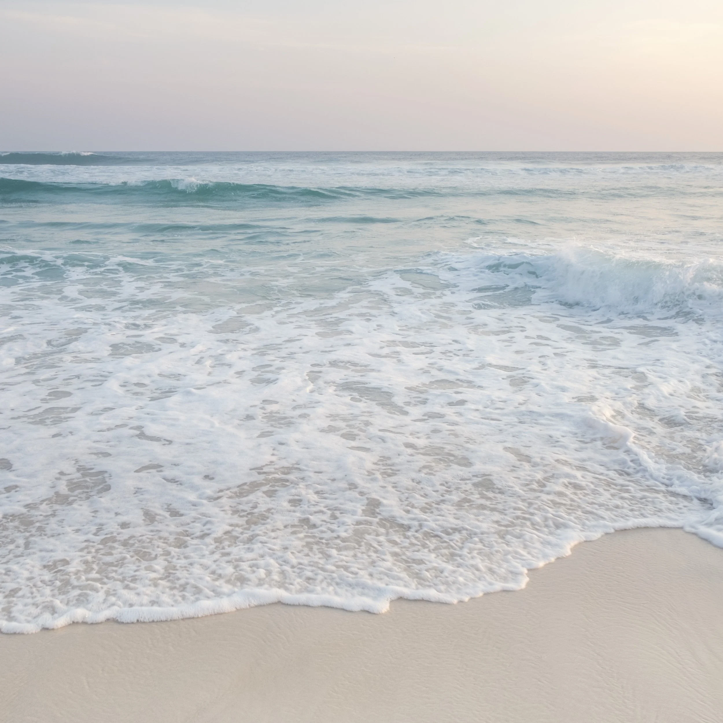 Oceano calmo no Rio de Janeiro com ondas leves tocando a areia clara sob luz suave, ideal para ambientes que pedem sensação de calma e horizonte limpo.