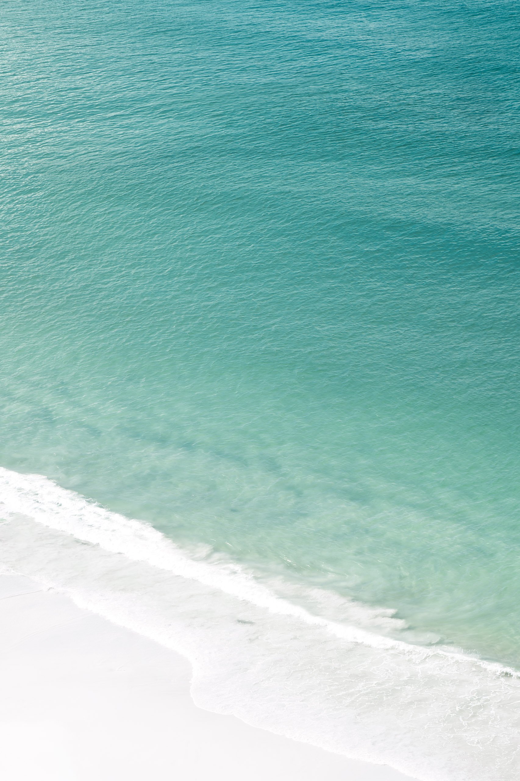 Mar turquesa visto de cima com onda suave chegando na areia branca, pensado para projetos de interiores que buscam leveza e cor natural.
