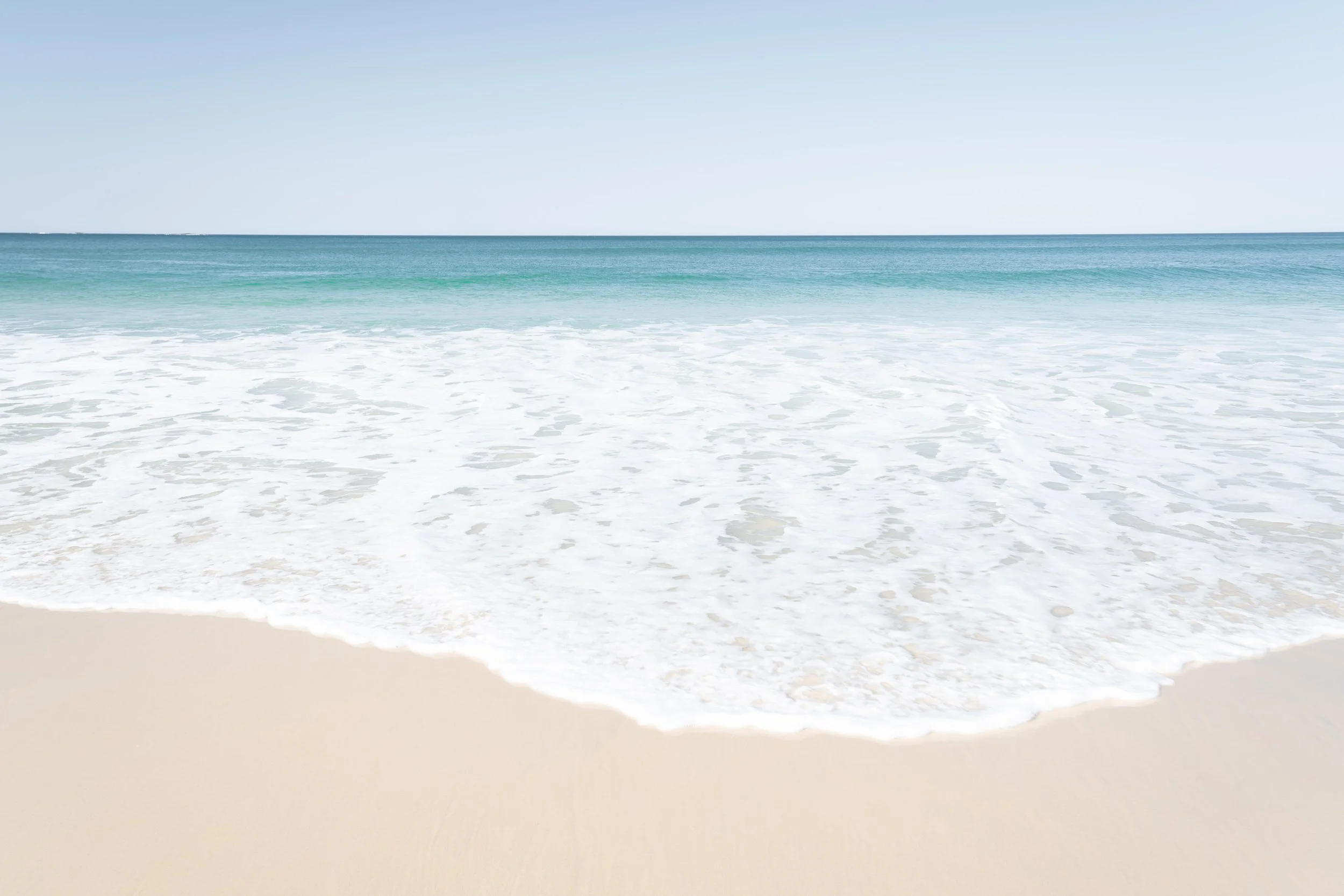 Mar calmo com água azul clara chegando suavemente na areia branca em um dia aberto no Rio de Janeiro, ideal para projetos de interiores que buscam leveza, silêncio visual e sensação de amplitude em salas, quartos e áreas de descanso.