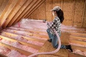 Person spraying insulation in an attic with pink insulation material.