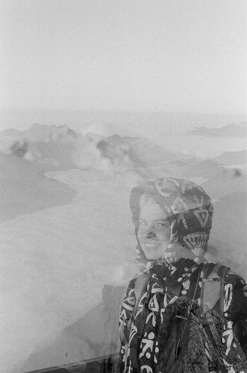 A person with a backpack and helmet standing on a mountain with a foggy mountain range in the background.