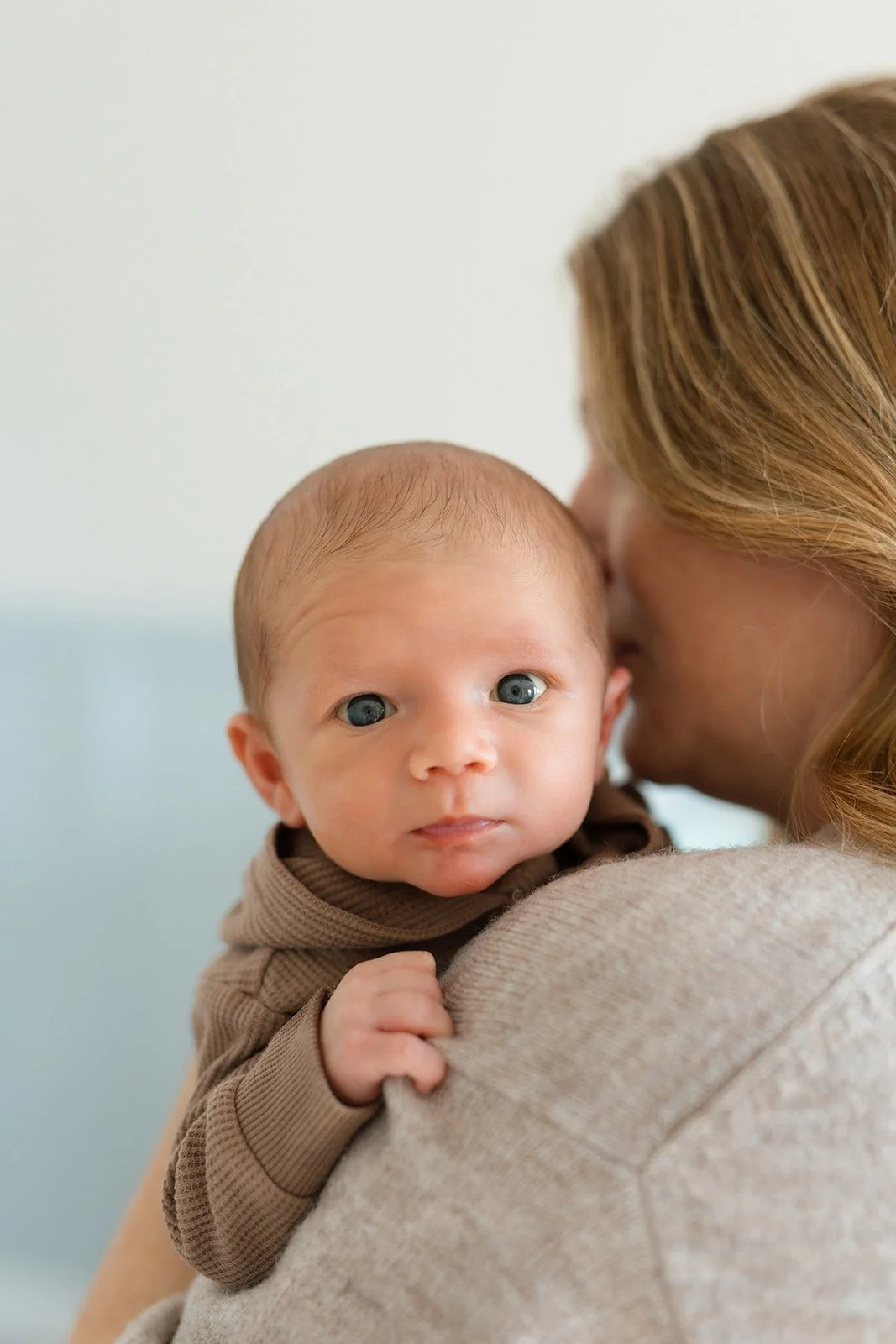 A woman holding a baby with blue eyes, close to her face, in a cozy setting.
