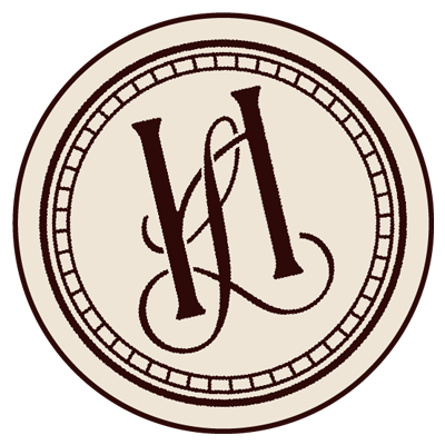 A circular logo with a beige background, featuring a dark brown decorative monogram in the center and a bordered edge.
