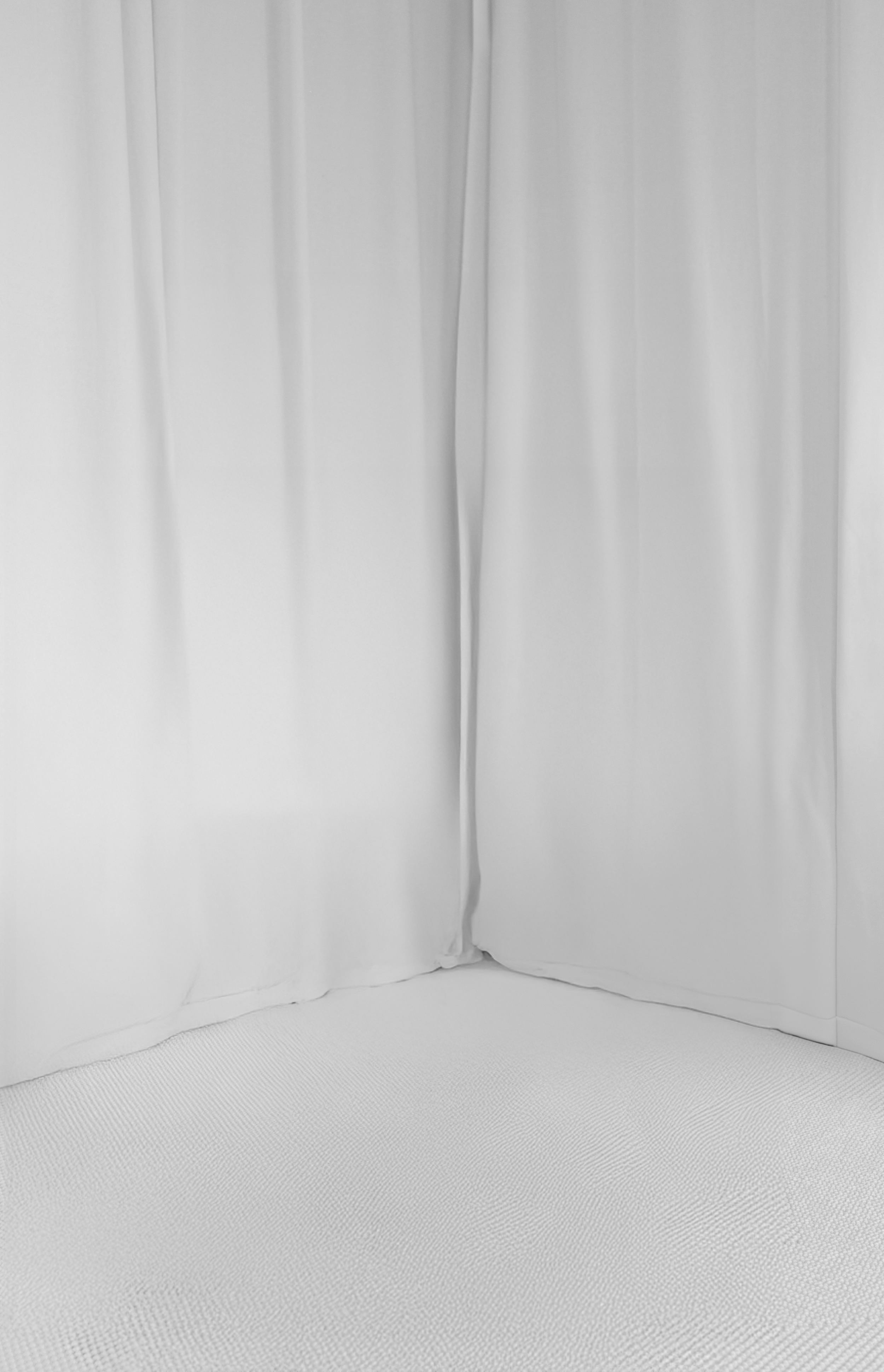 White curtains hanging down with a white textured ground.