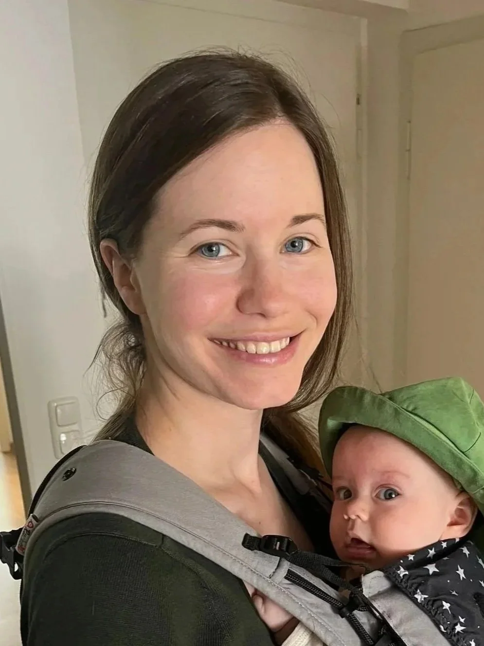 Die Kursleiterin, Regine Frieling, trägt ihre Tochter in einer Trage und lächelt.