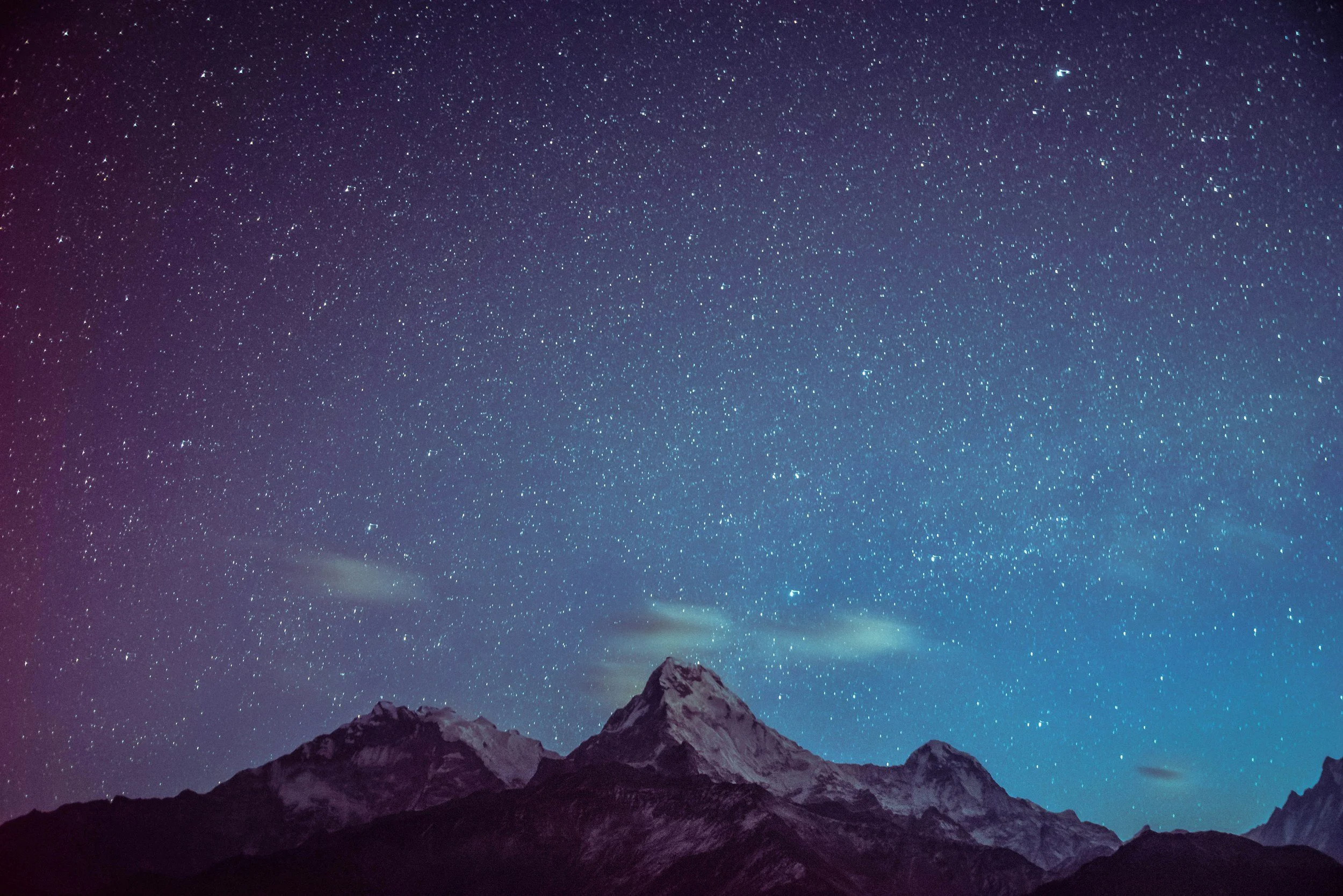 Night sky filled with stars above snow-capped mountain peaks.