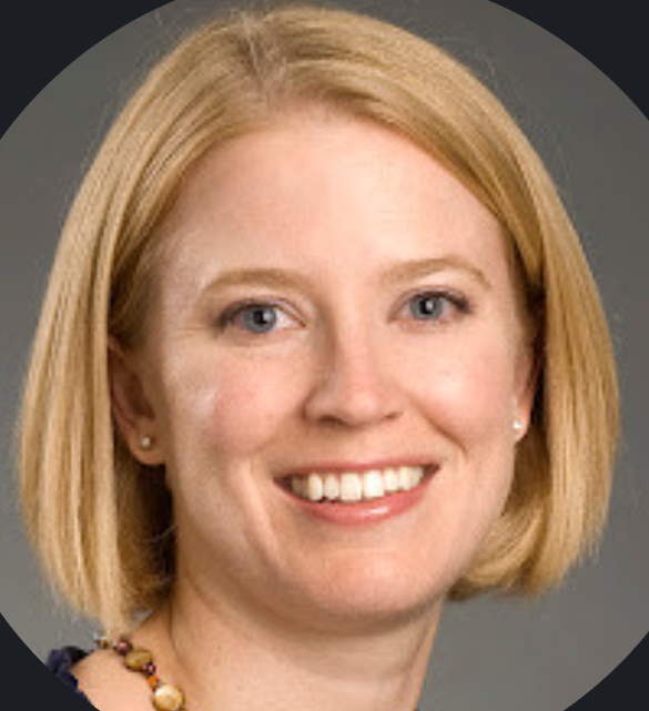 A portrait of a woman with blonde hair, blue eyes, and a friendly smile, wearing pearl earrings and a colorful beaded necklace.