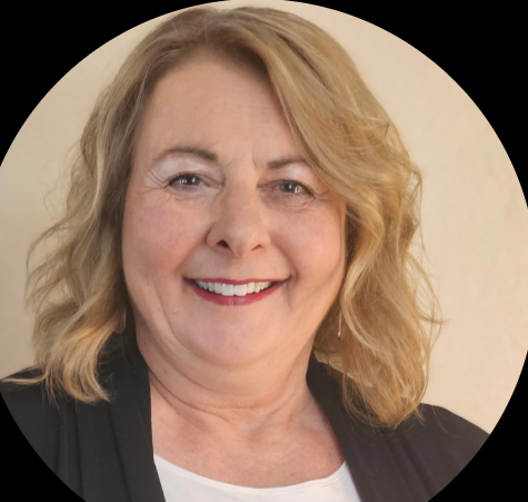 A smiling middle-aged woman with wavy blonde hair, wearing a black top, against a neutral background.