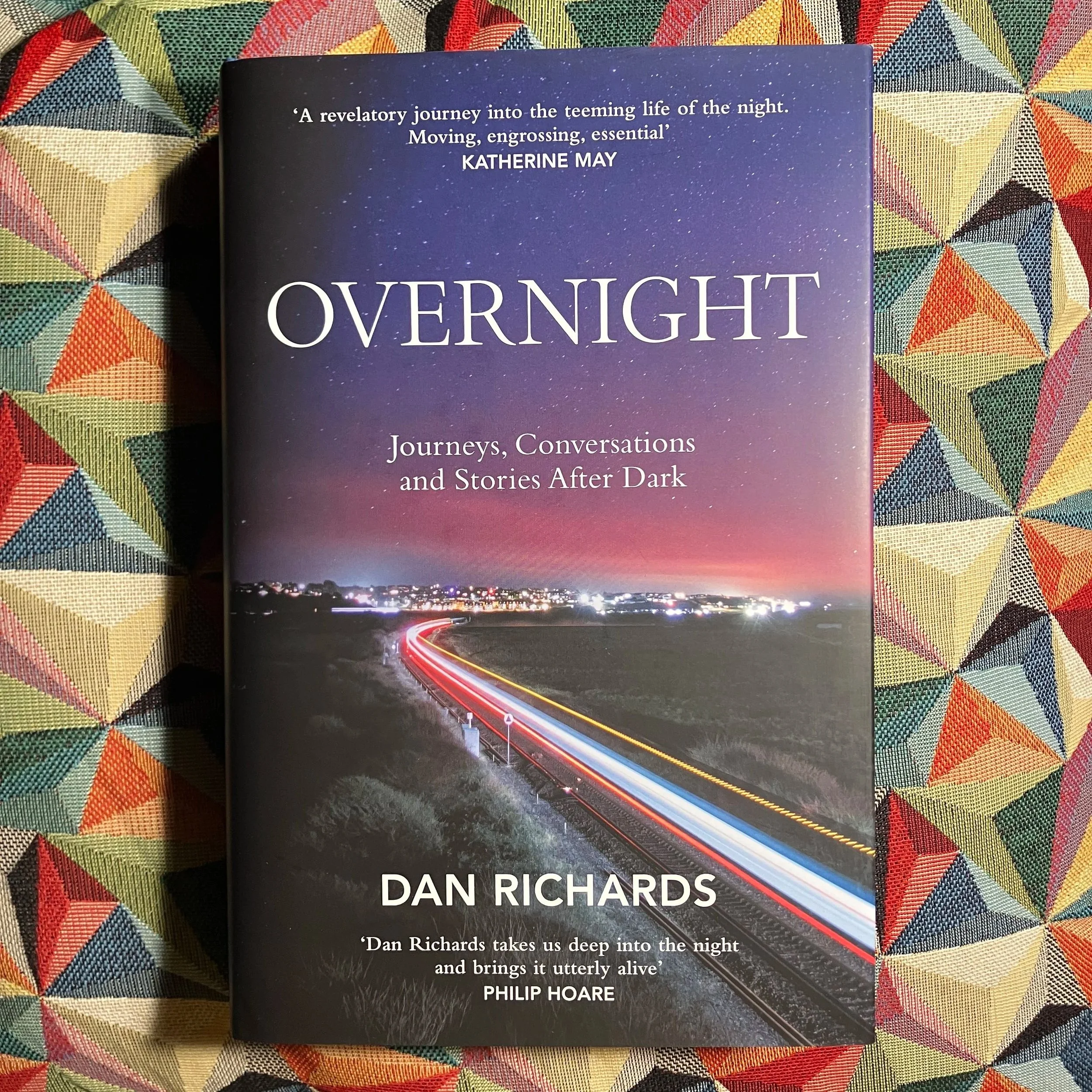 Book titled "Overnight: Journeys, Conversations and Stories After Dark" by Dan Richards, with a cover image of a nocturnal landscape featuring a passing train, set against a twilight sky. Published by Canongate Books in 2025.