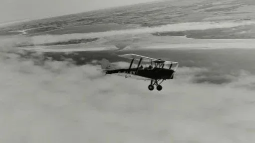Small vintage biplane flying through clouds in black and white.