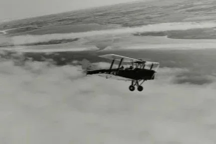 A small Tiger Moth airplane flying above thick clouds in black and white.