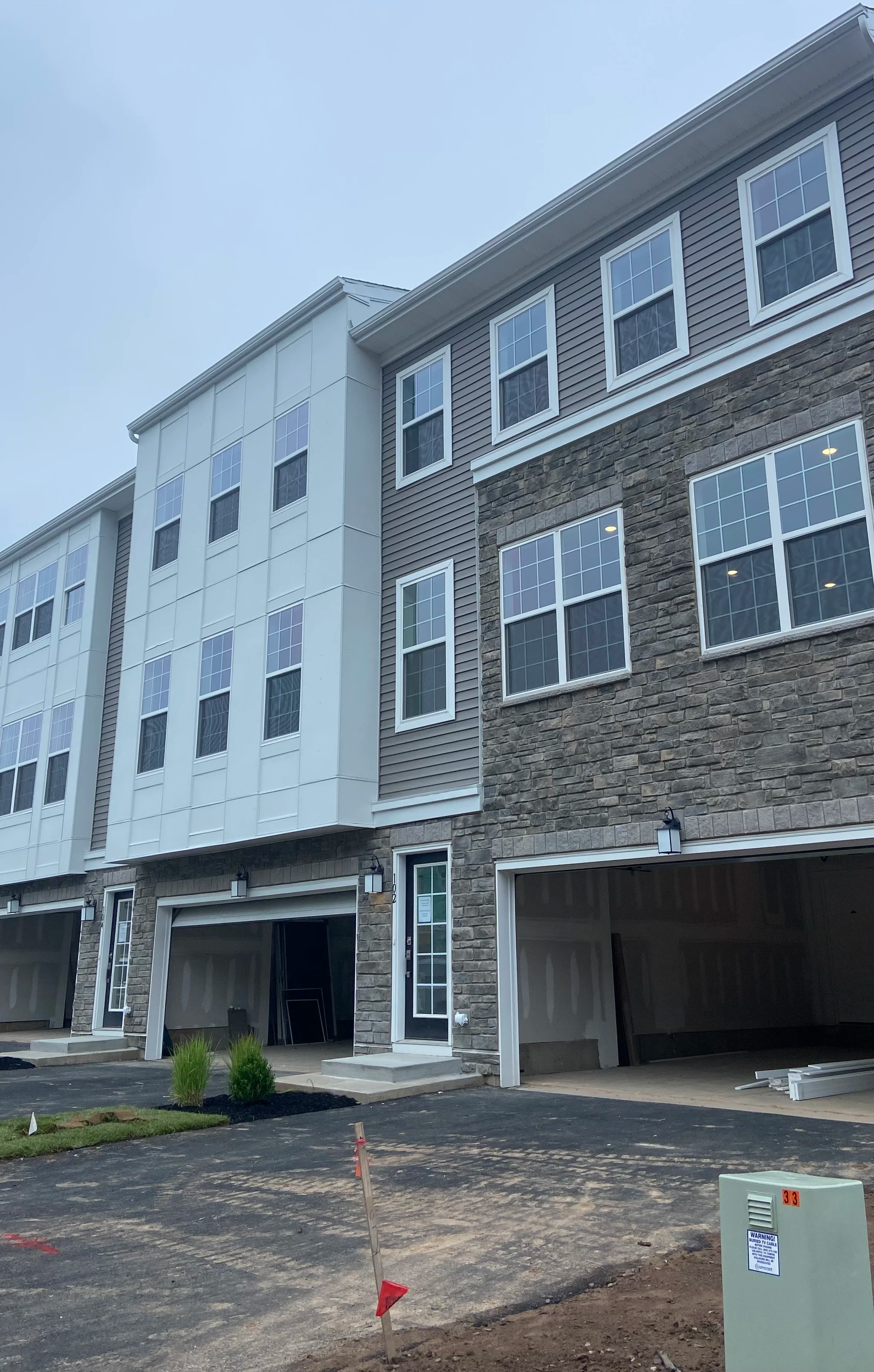 Exterior view of new multi-story townhouse or apartment building under construction, with stone and siding facade, multiple windows, and open garages at ground level.