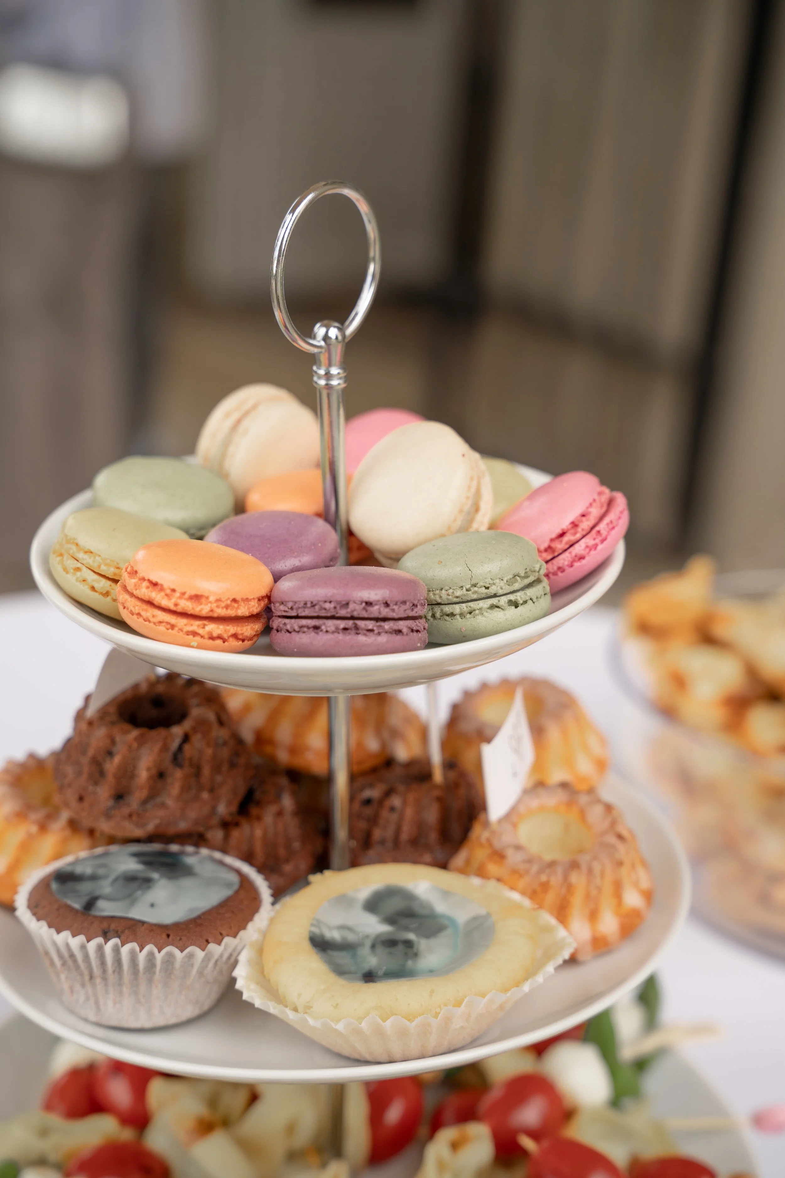 Ein mehrstöckiges Desserttablett mit bunten Macarons, Cupcakes und anderen Gebäcksorten auf einem weißen Tisch.