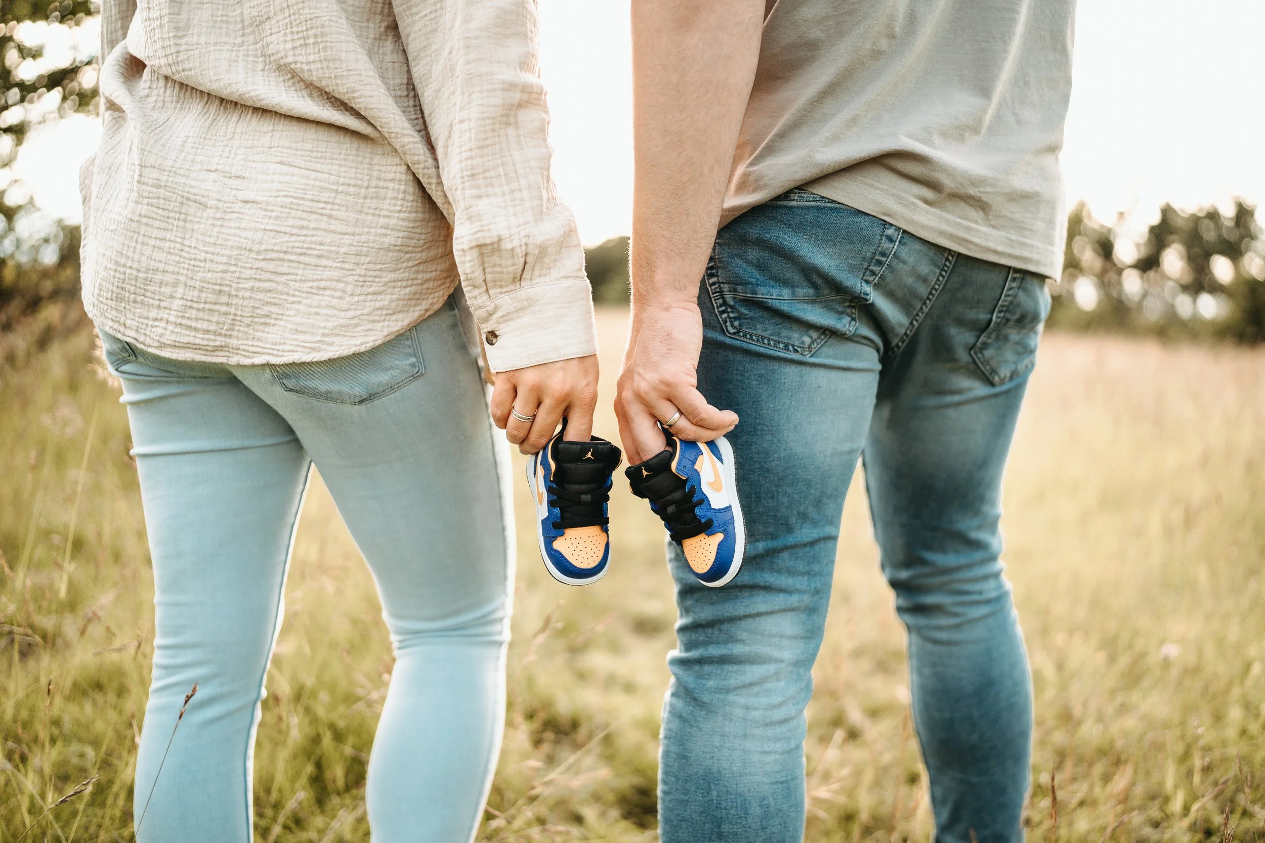 Ein Paar hält in einer Wiese kleine Turnschuhe.