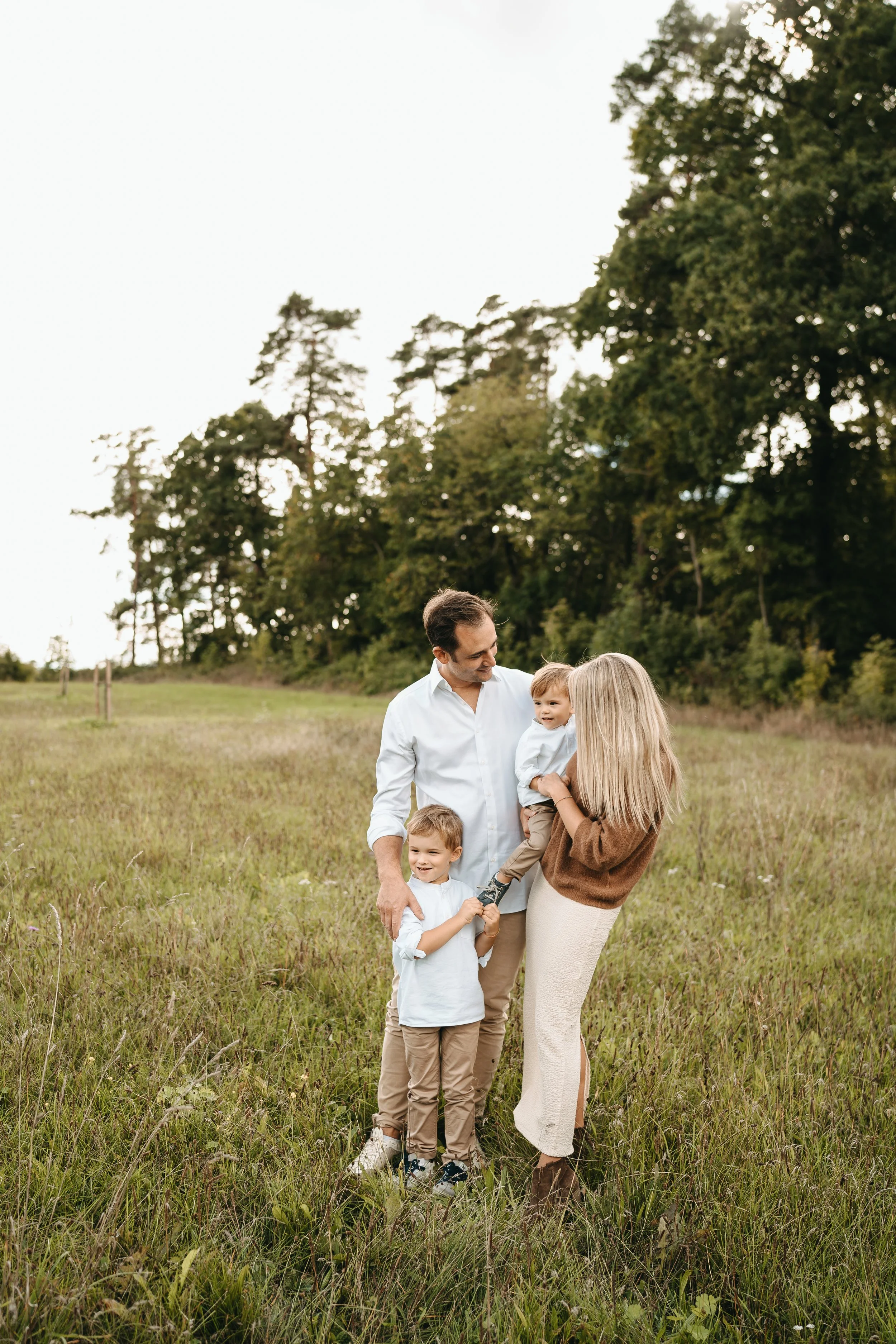 Familie mit vier Mitgliedern im offenen Feld, umgeben von Bäumen, fröhlich und beim Spielen.