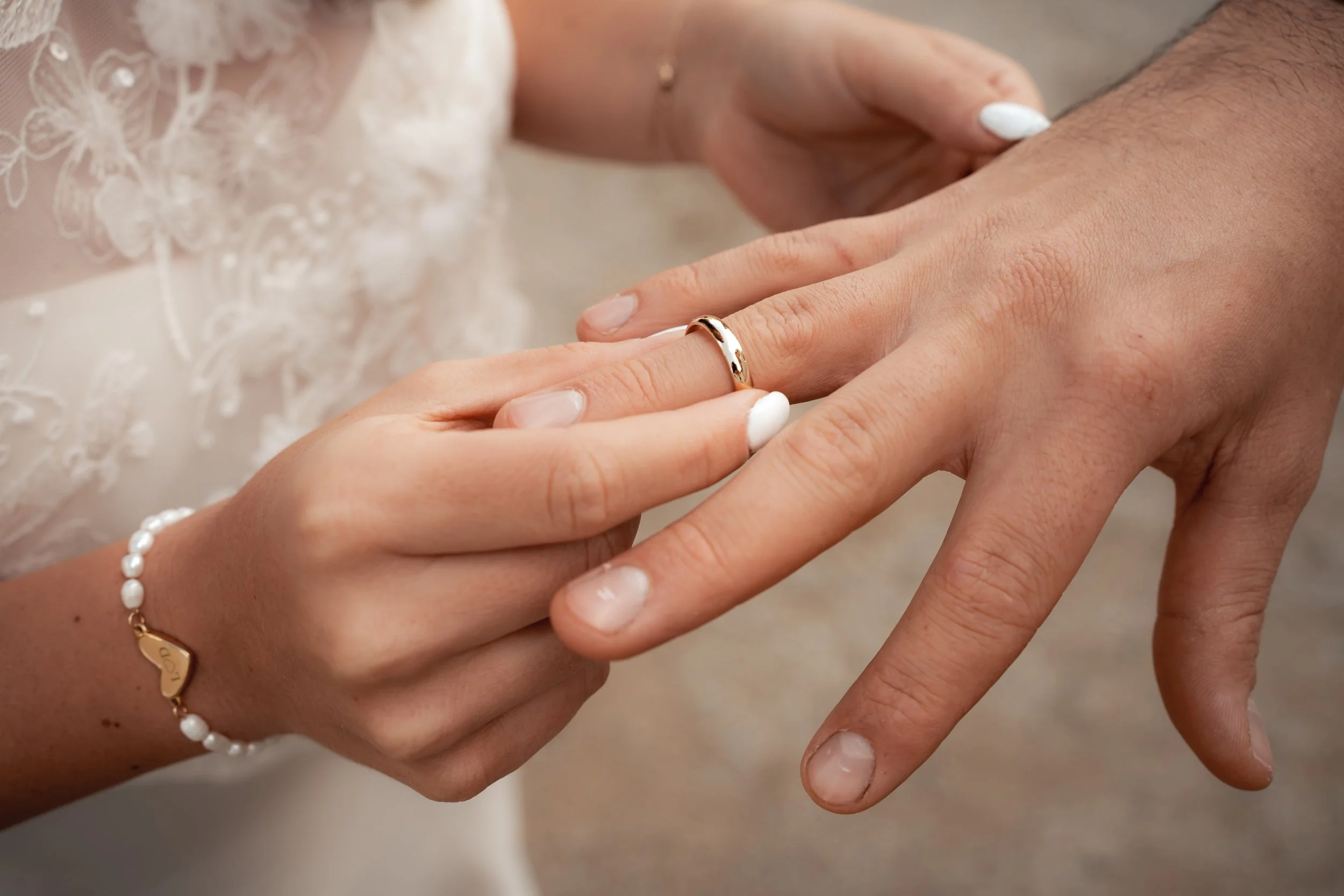 Eine Frau steckt einem Mann einen goldenen Ehering an den Finger, während sie eine weiße Kleiderjacke trägt.
