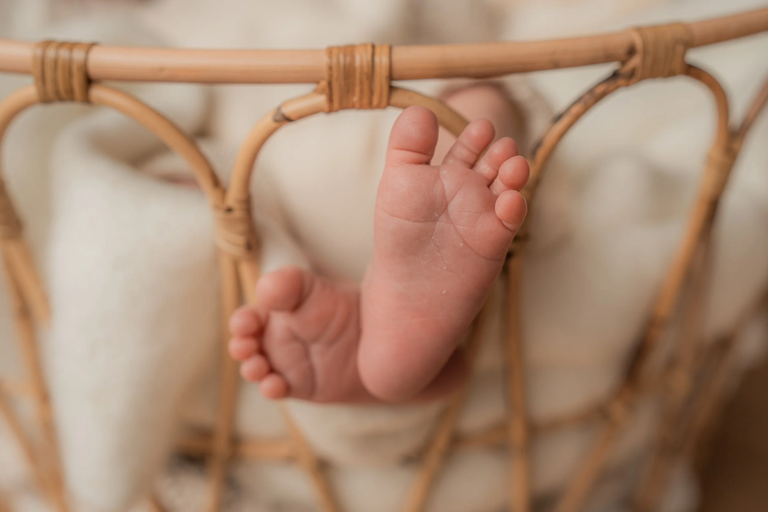 Nahaufnahme eines winzigen Babyfußes, der aus einem Korb herausragt.