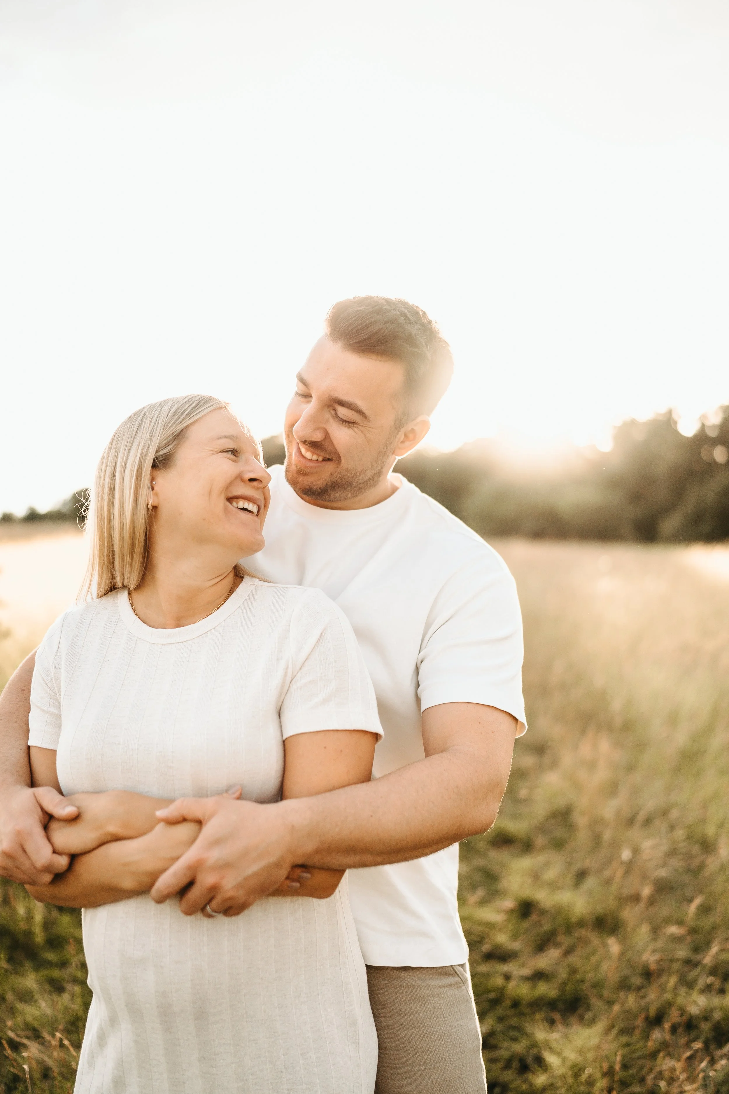 Ein glückliches Paar umarmt sich in einem Feld bei Sonnenuntergang.
