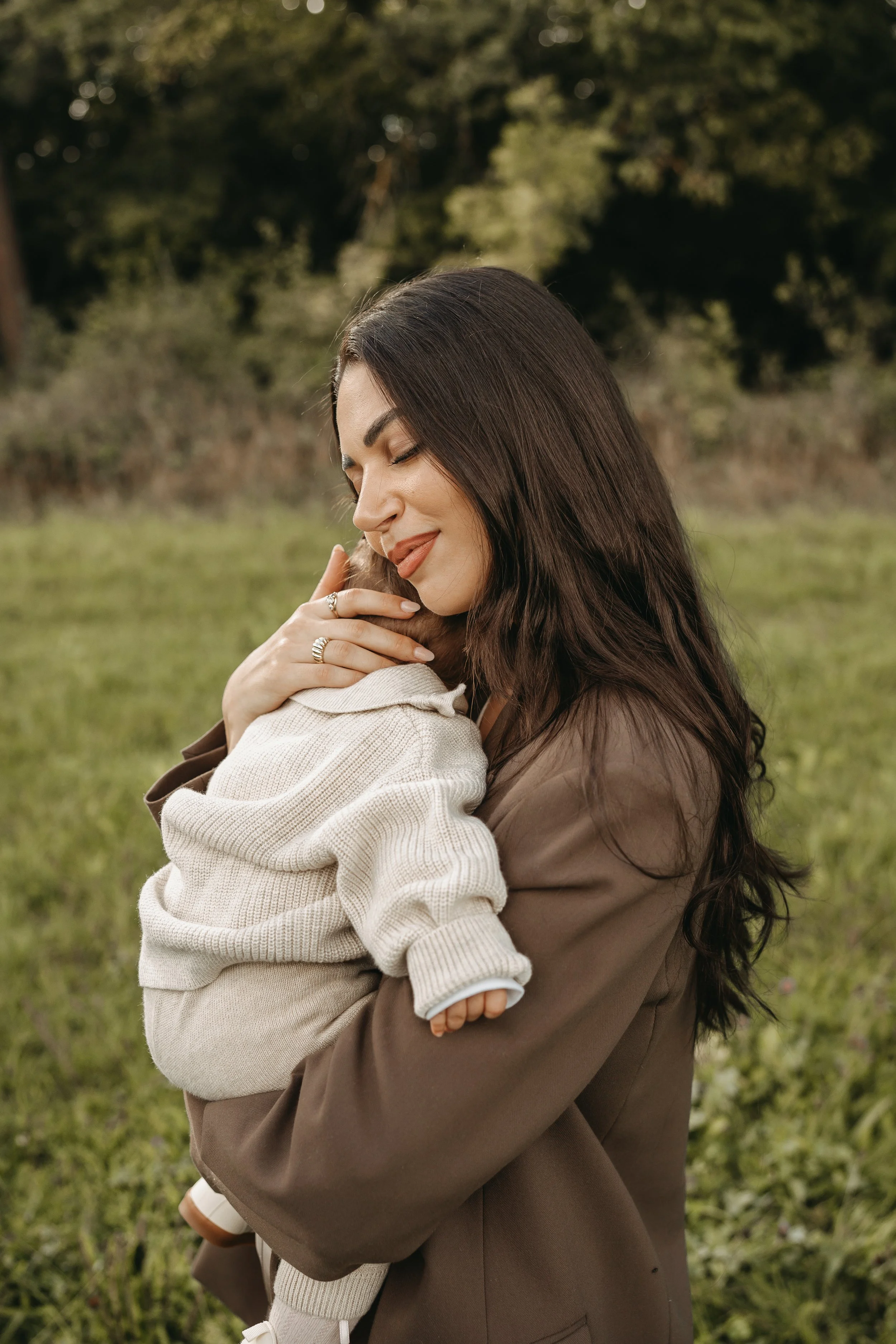Eine Frau umarmt ein kleines Kind draußen im Grünen bei Sonnenuntergang.