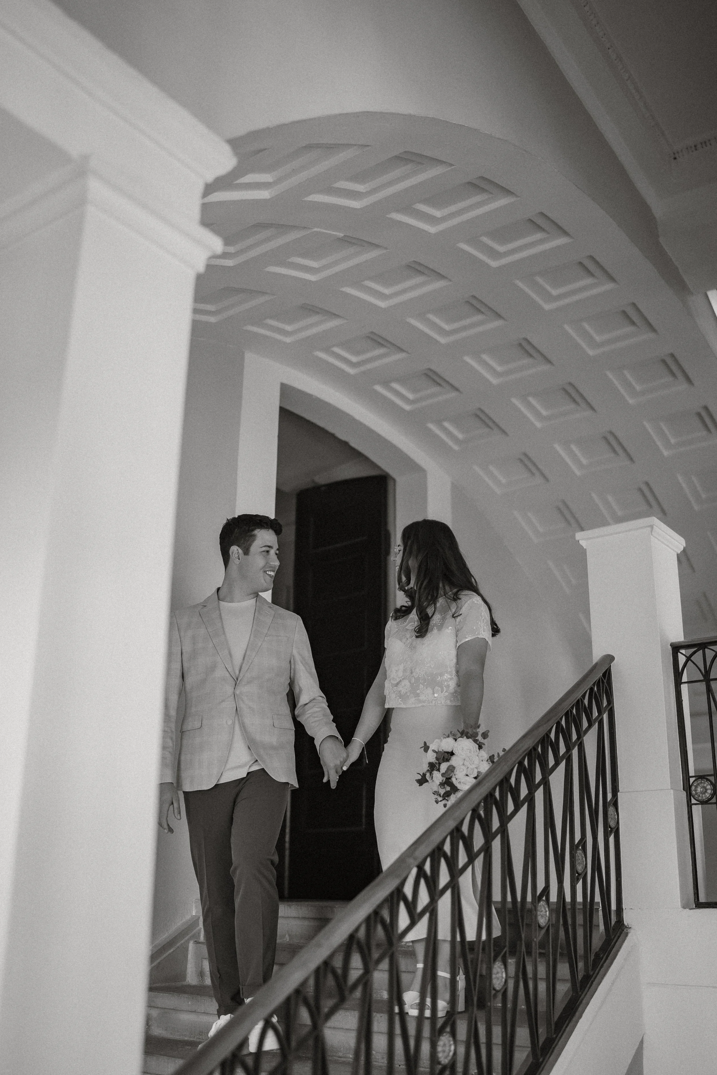 Ein glückliches Paar auf der Treppe eines eleganten Gebäudes, die Frau hält einen Blumenstrauß.