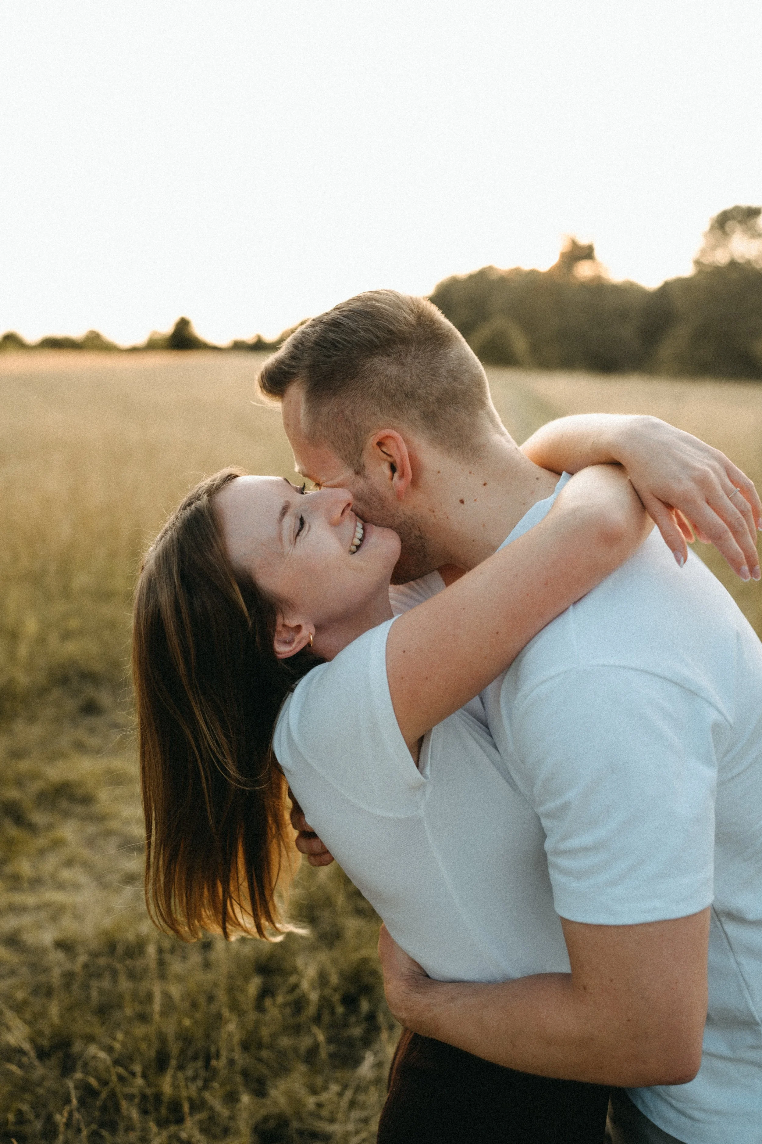 Ein Paar umarmt sich liebevoll im Freien bei Sonnenuntergang in einer Feldlandschaft.