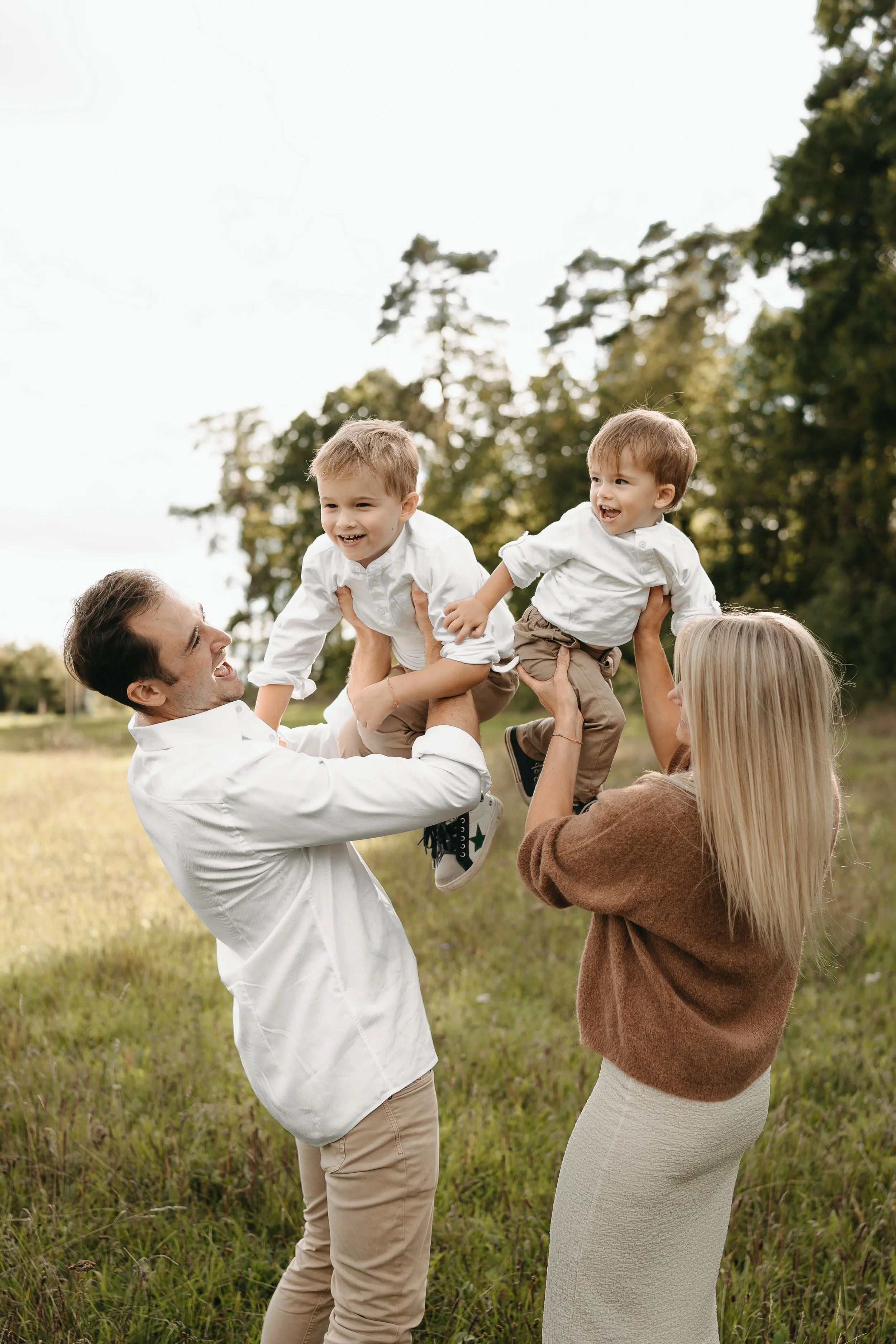Familie mit zwei kleinen Jungen, die auf einer Wiese im Freien spielen und lachen.
