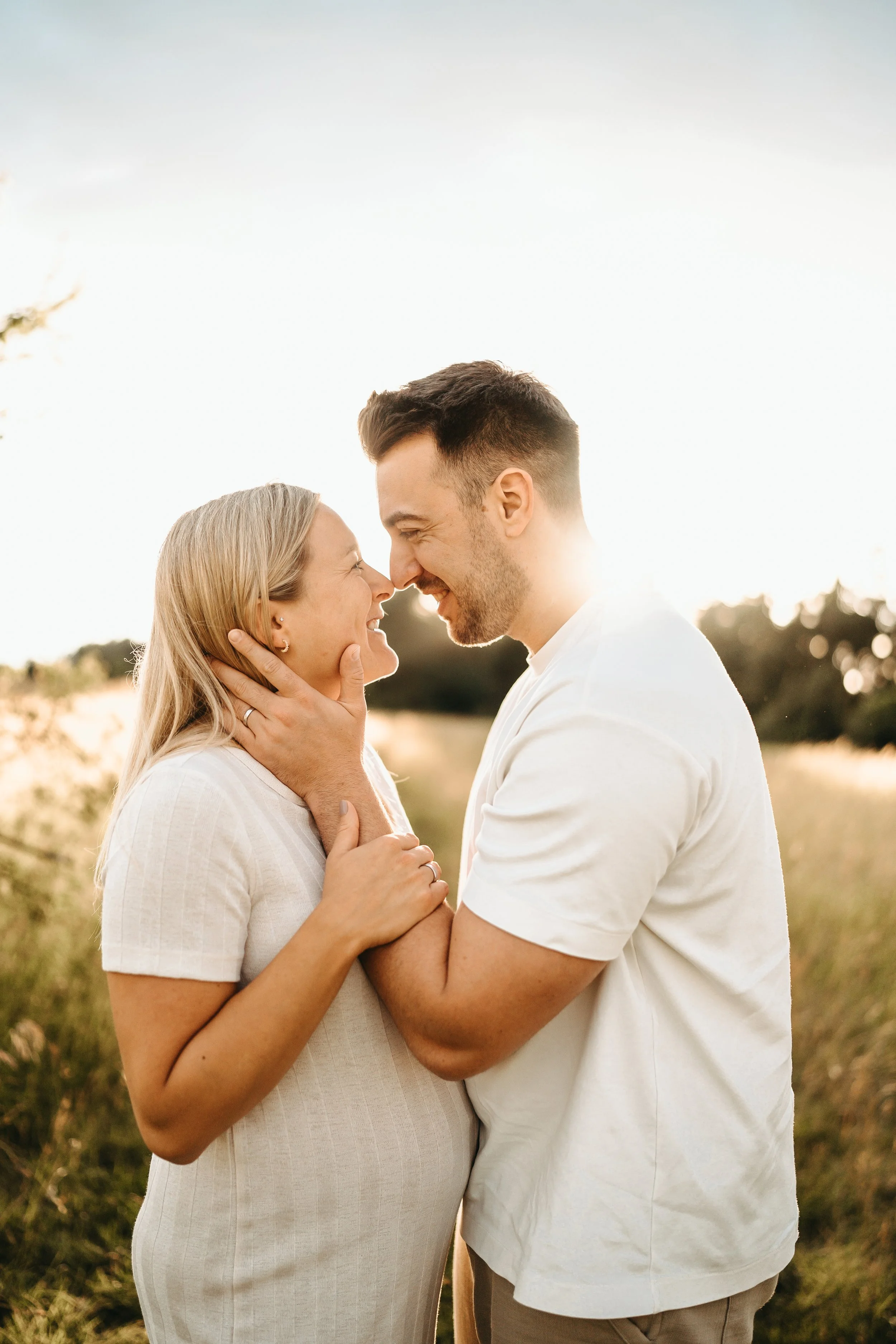 Ein glückliches Paar steht in einem Feld bei Sonnenuntergang, sich liebevoll berührend.