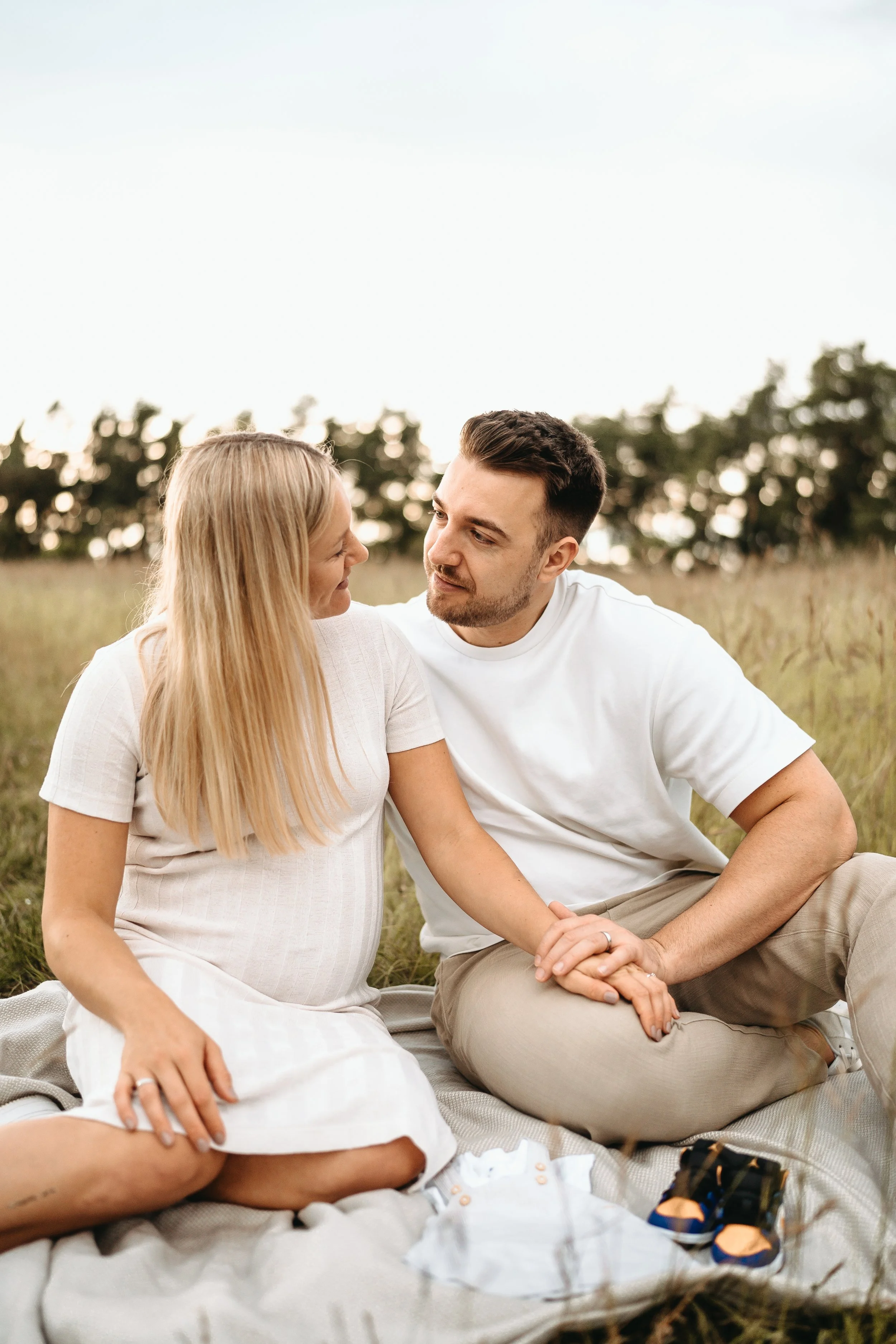 Ein Paar sitzt im Freien auf einer Decke, umgeben von Natur, und schaut sich liebevoll an.