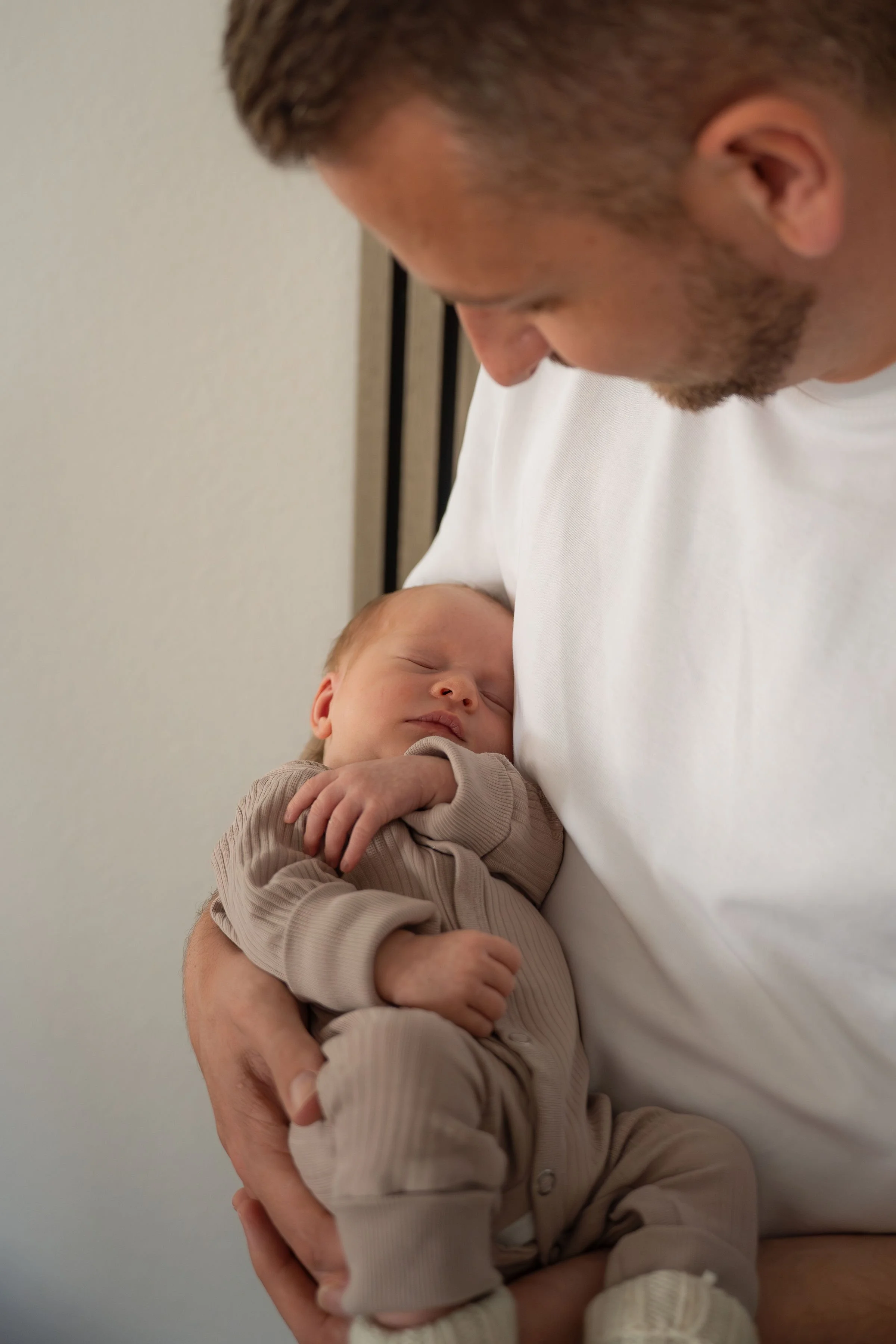 Ein Mann hält ein schlafendes Baby in seinen Armen, das gegen seine Brust liegt.