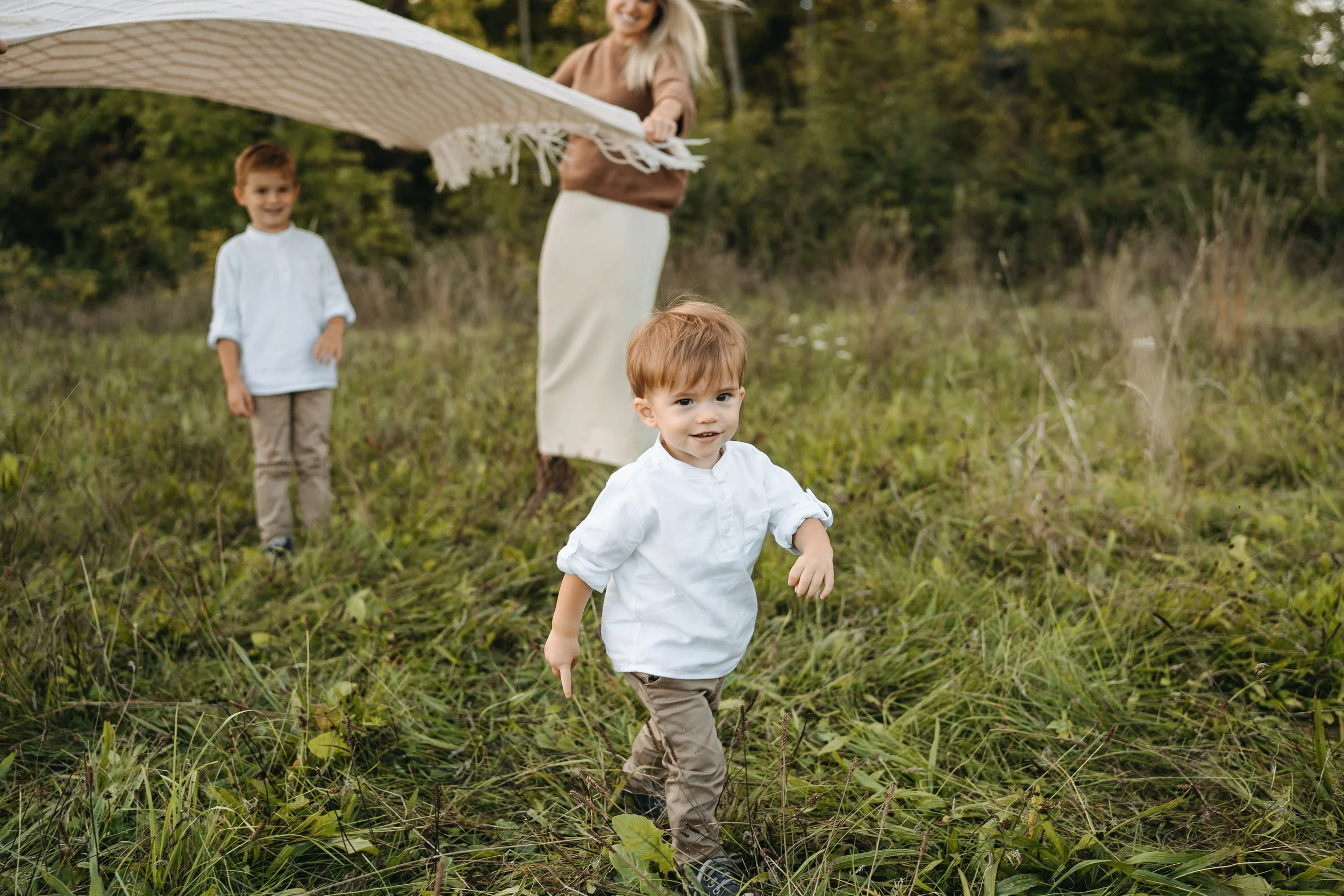 Ein Mann und zwei Kinder im Grünen, eines läuft voraus, während der Mann ein Tuch hält, vermutlich beim Picknick im Freien.