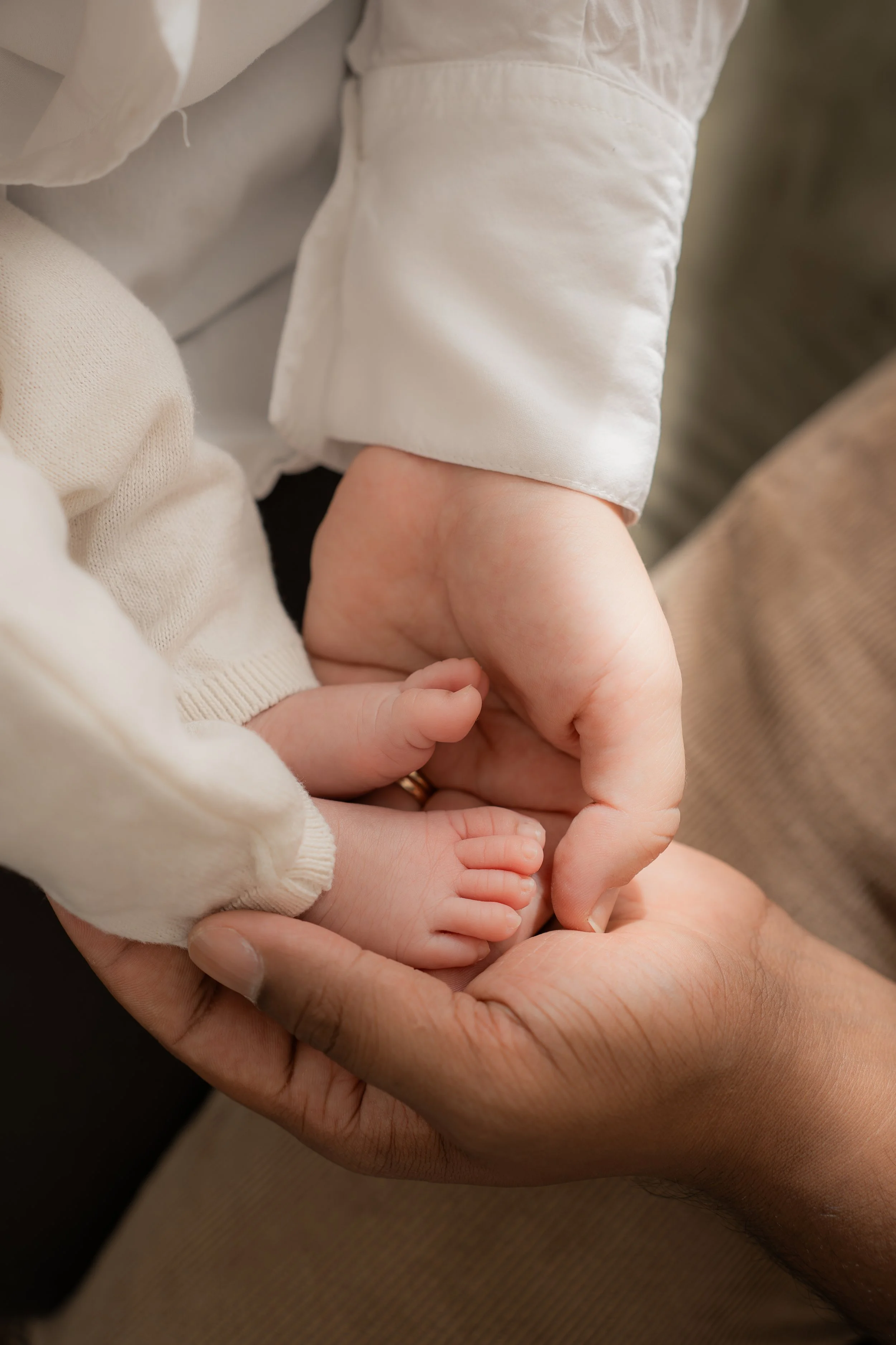 Nahaufnahme einer Hand, die eine kleine Babyhand hält, während das Baby auf dem Arm eines Erwachsenen liegt.