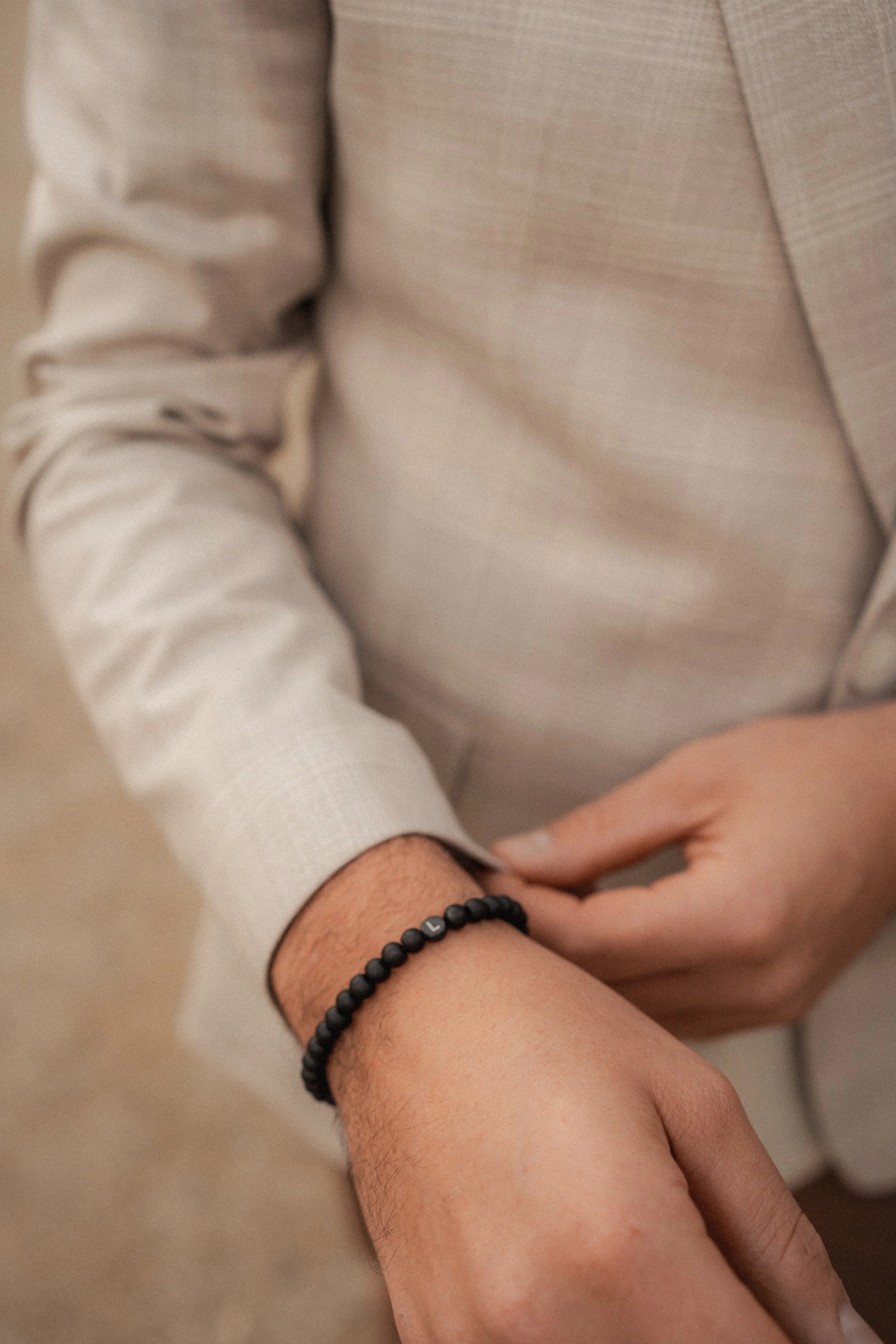 Nahaufnahme eines Mannes, der an seinem Handgelenk eine schwarze Armbanduhr trägt, in einem hellen Anzug.