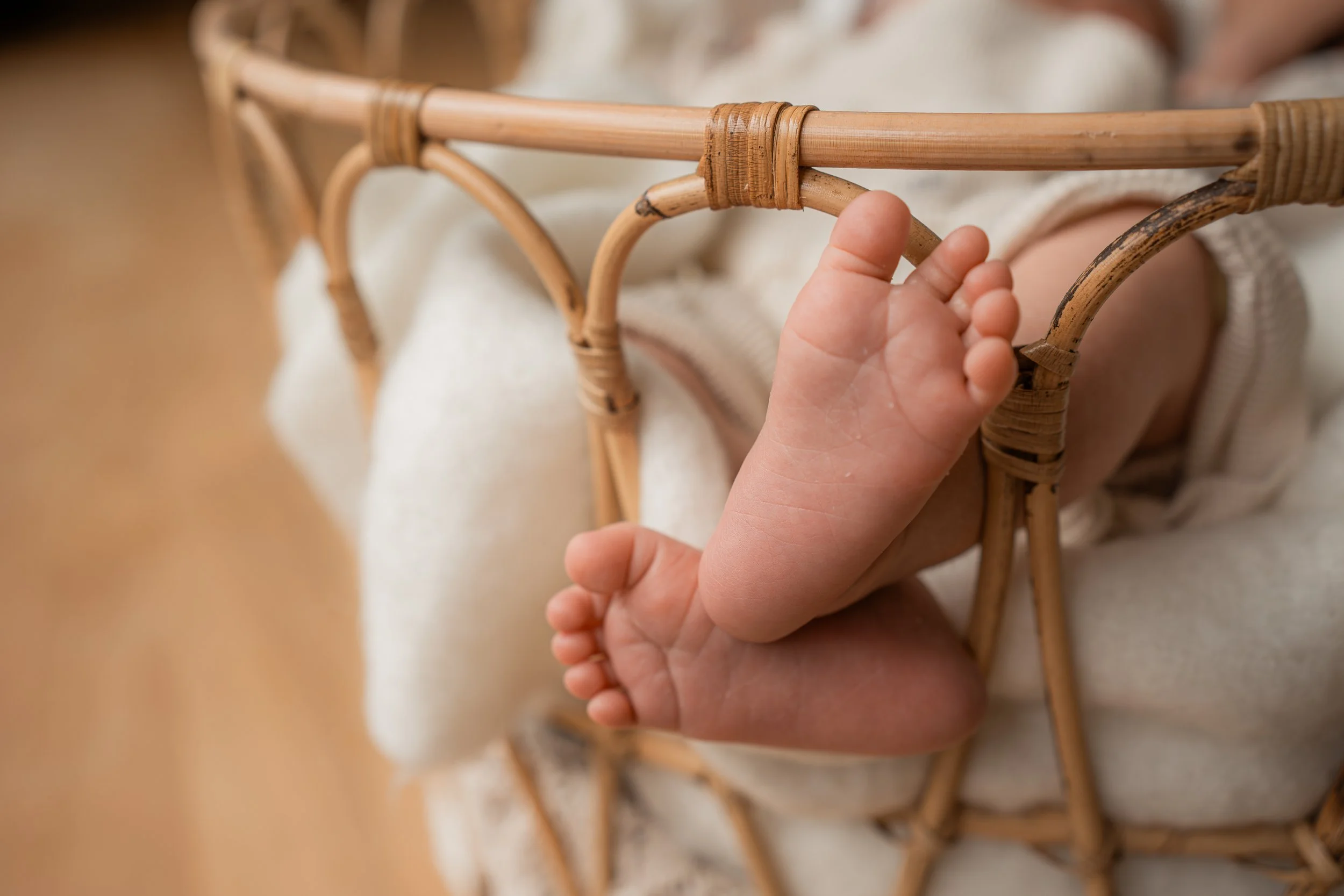 Nahaufnahme eines Säuglings, der in einem Korb liegt, mit einem Fokus auf den kleinen Füßen und der Hand des Babys.